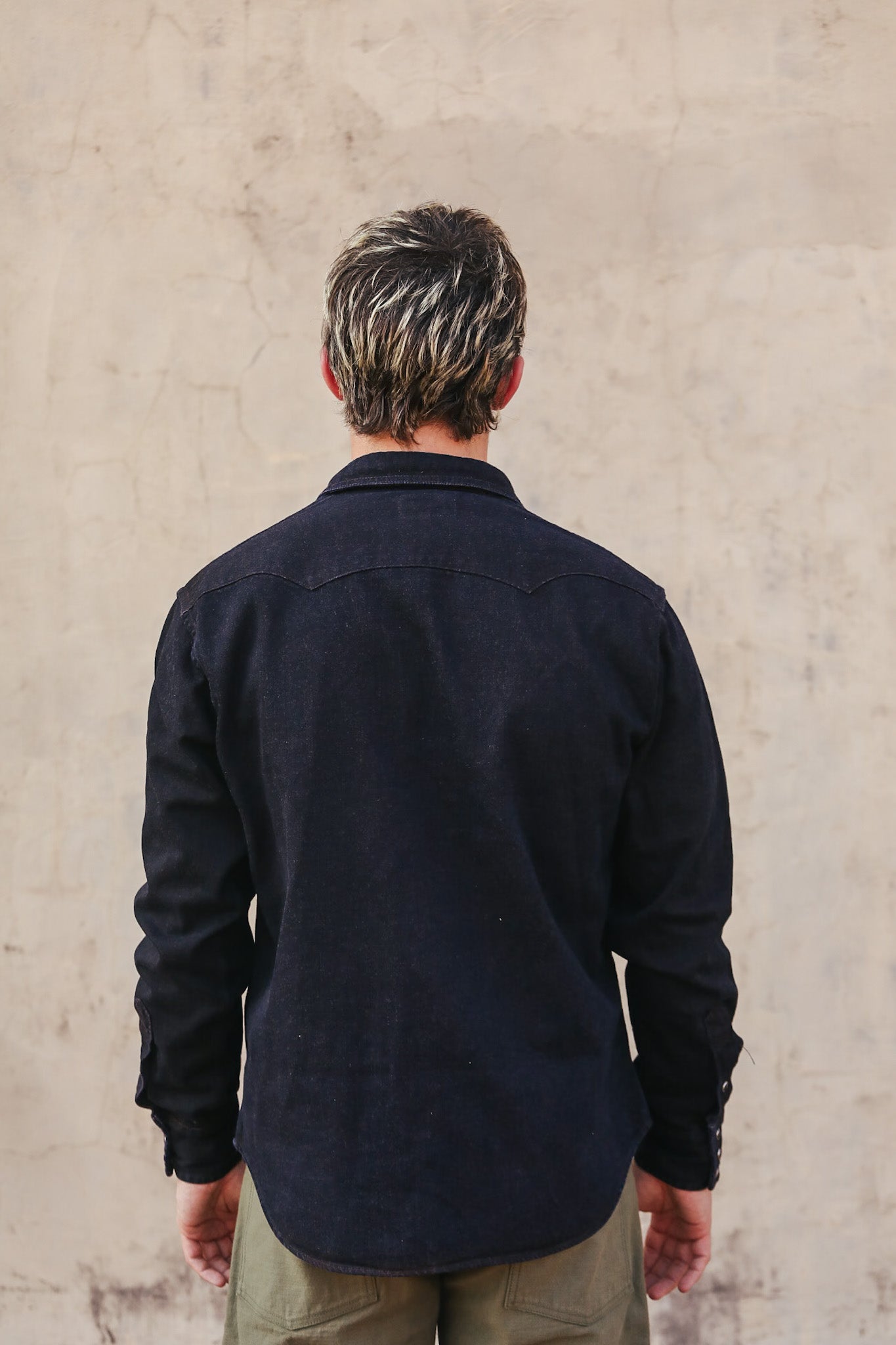 Person wearing a dark jacket standing against a plain wall