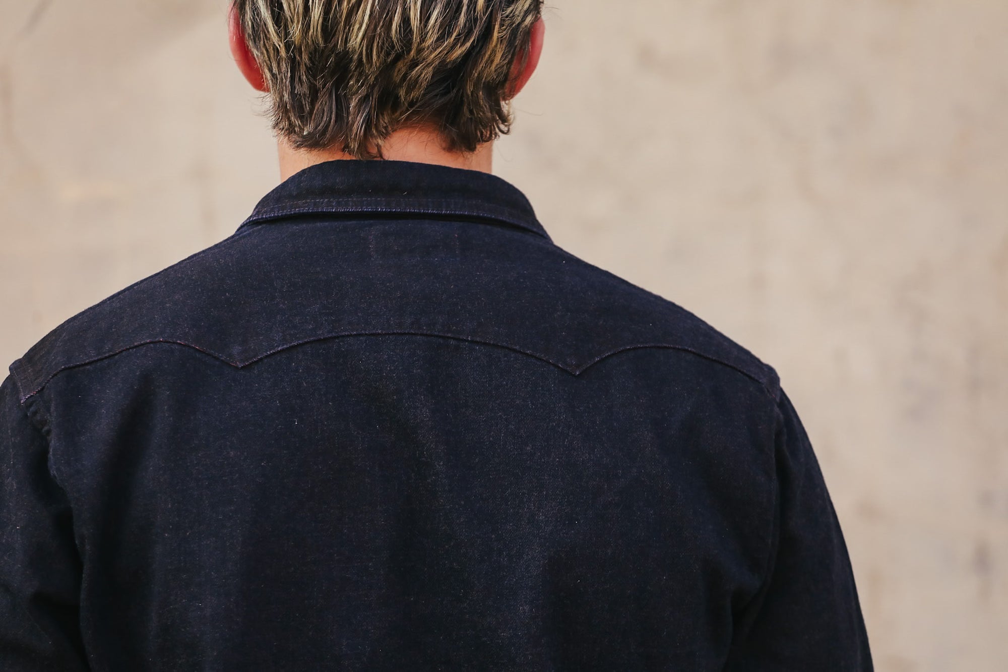 Person wearing a dark denim jacket with a neutral background