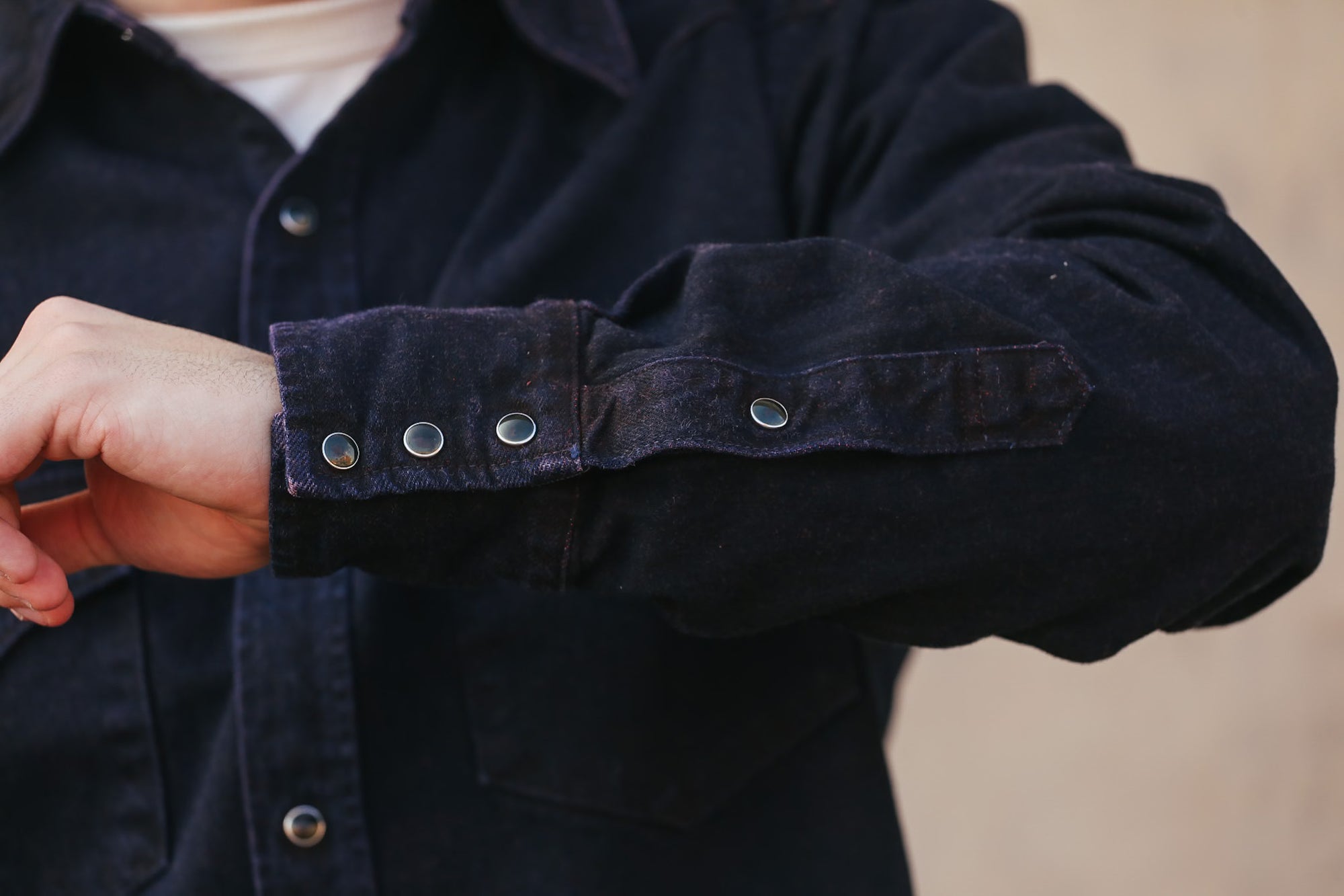 Close-up of a person wearing a dark jacket with button details on a beige background