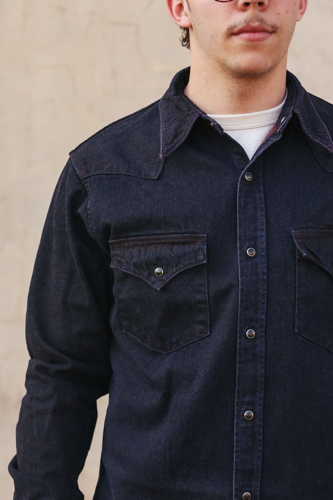Person wearing a dark denim shirt against a beige background