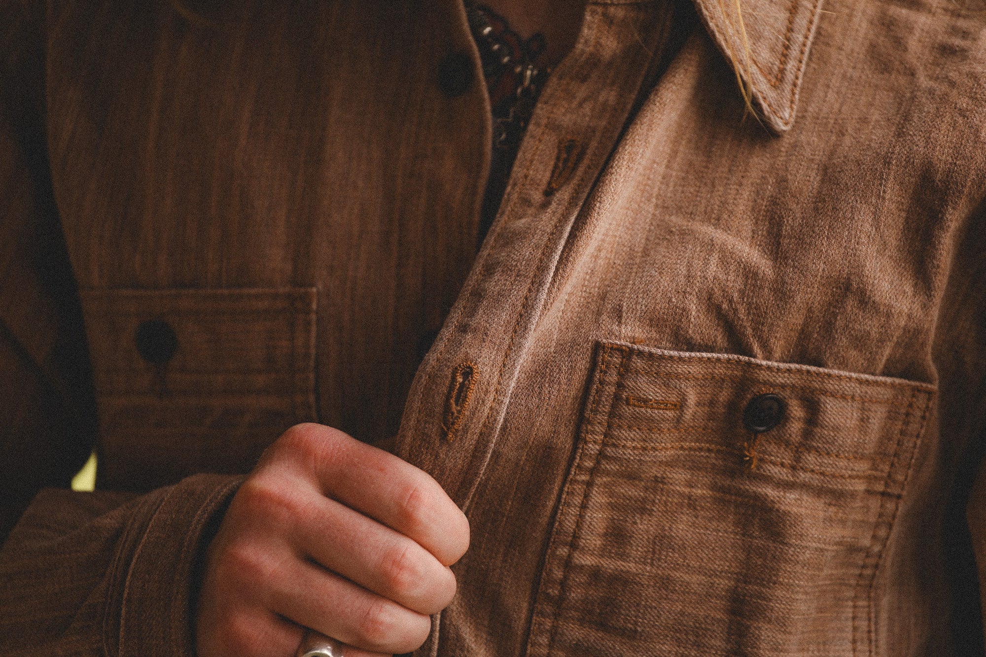 Close-up of a person wearing a brown jacket with a focus on the hand and jacket details.