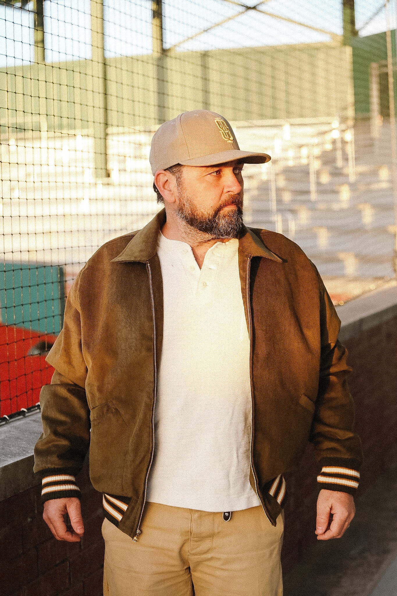 Man wearing a brown varsity jacket and beige cap outdoors