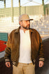 Man wearing a brown varsity jacket and beige cap outdoors
