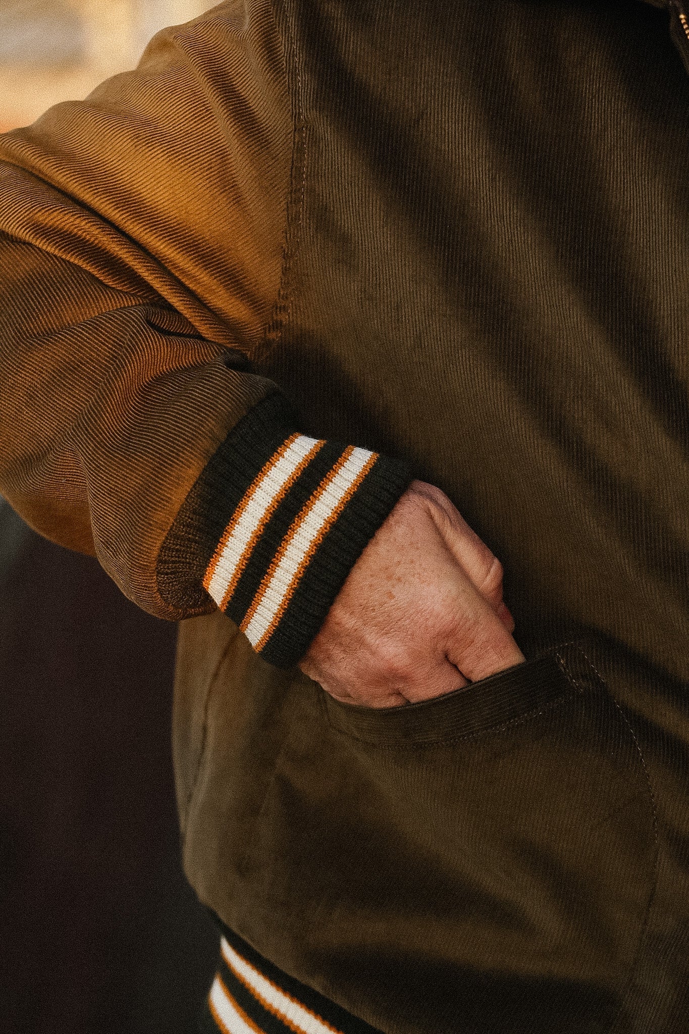 Close-up of a person wearing a brown jacket with striped cuffs.
