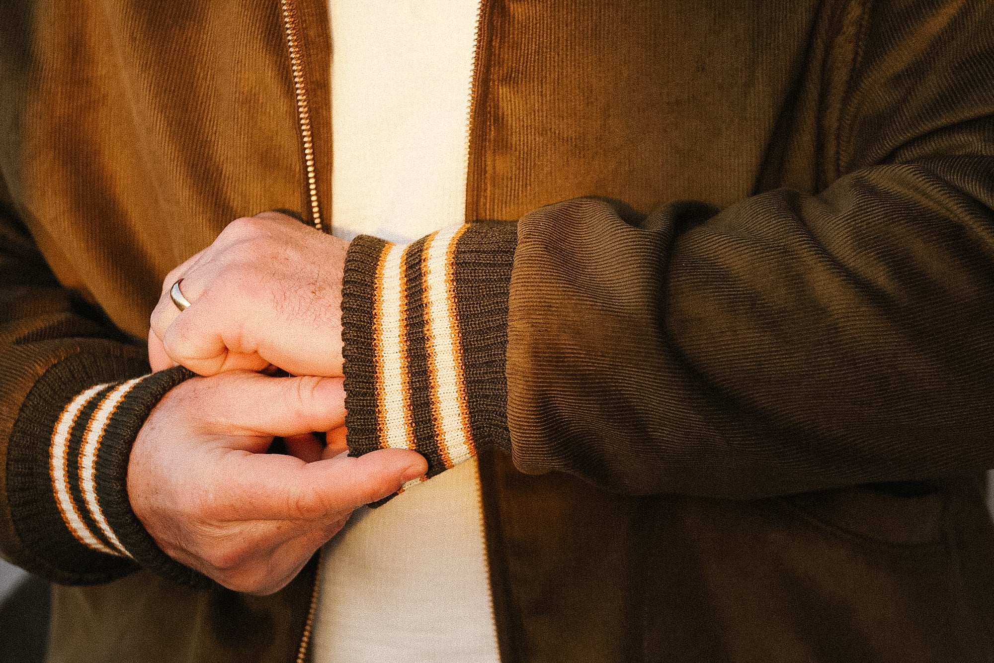 Close-up of a person wearing a brown jacket with striped cuffs.