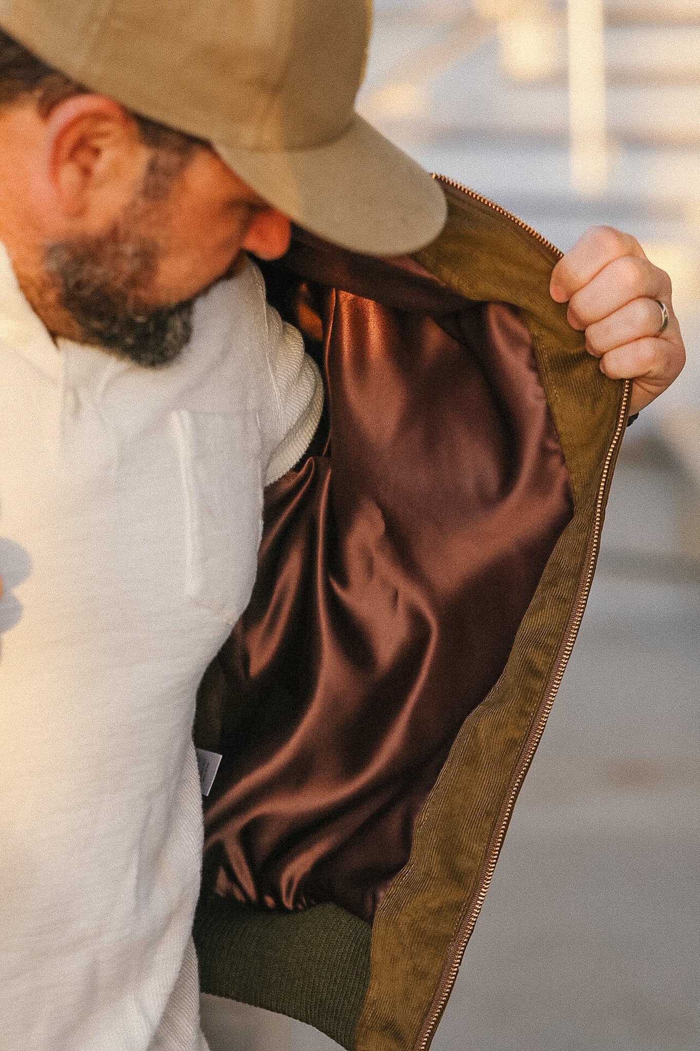 Man holding open a brown jacket with a blurred background