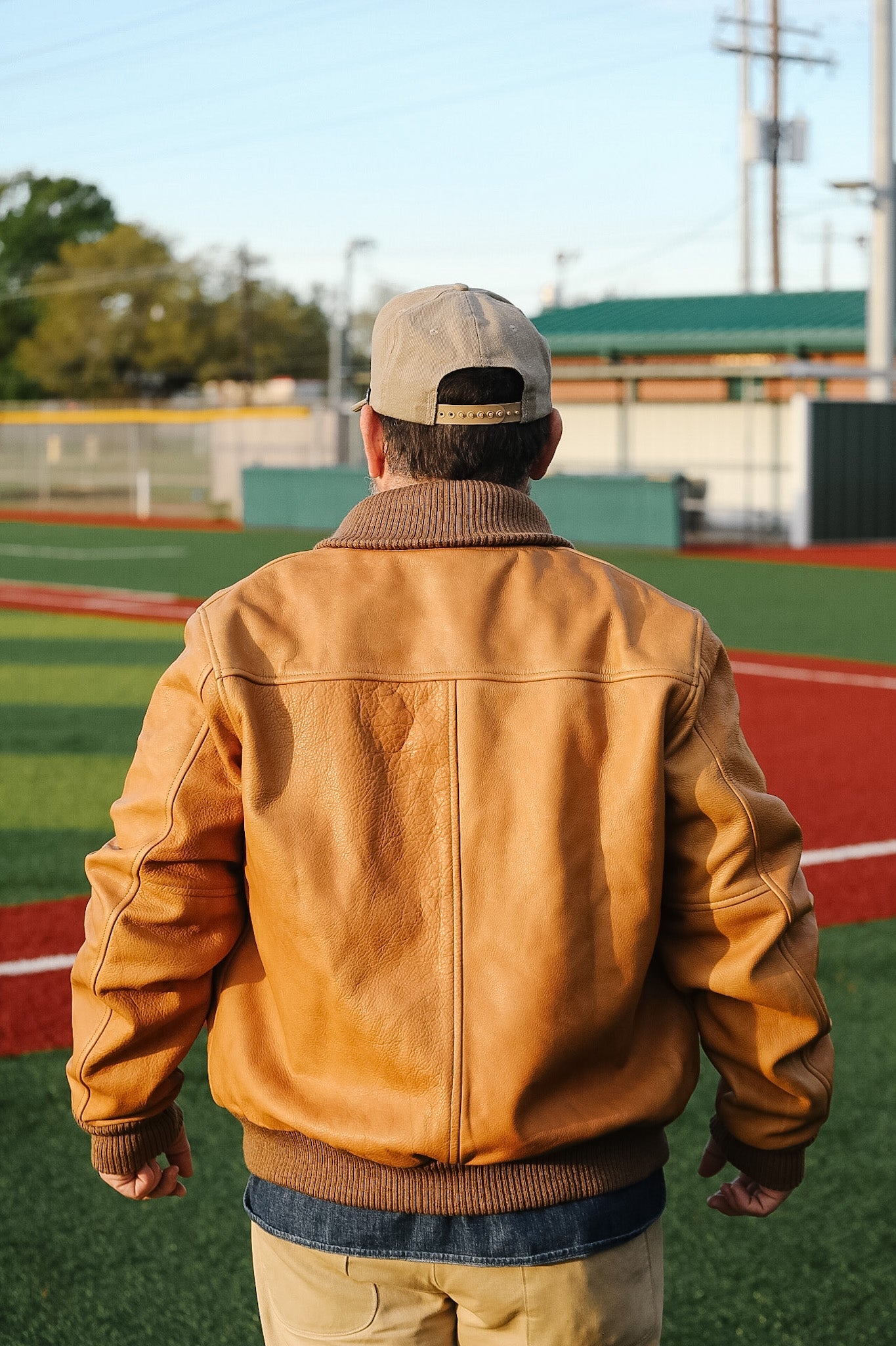 Person wearing a brown leather jacket and cap on a sports field