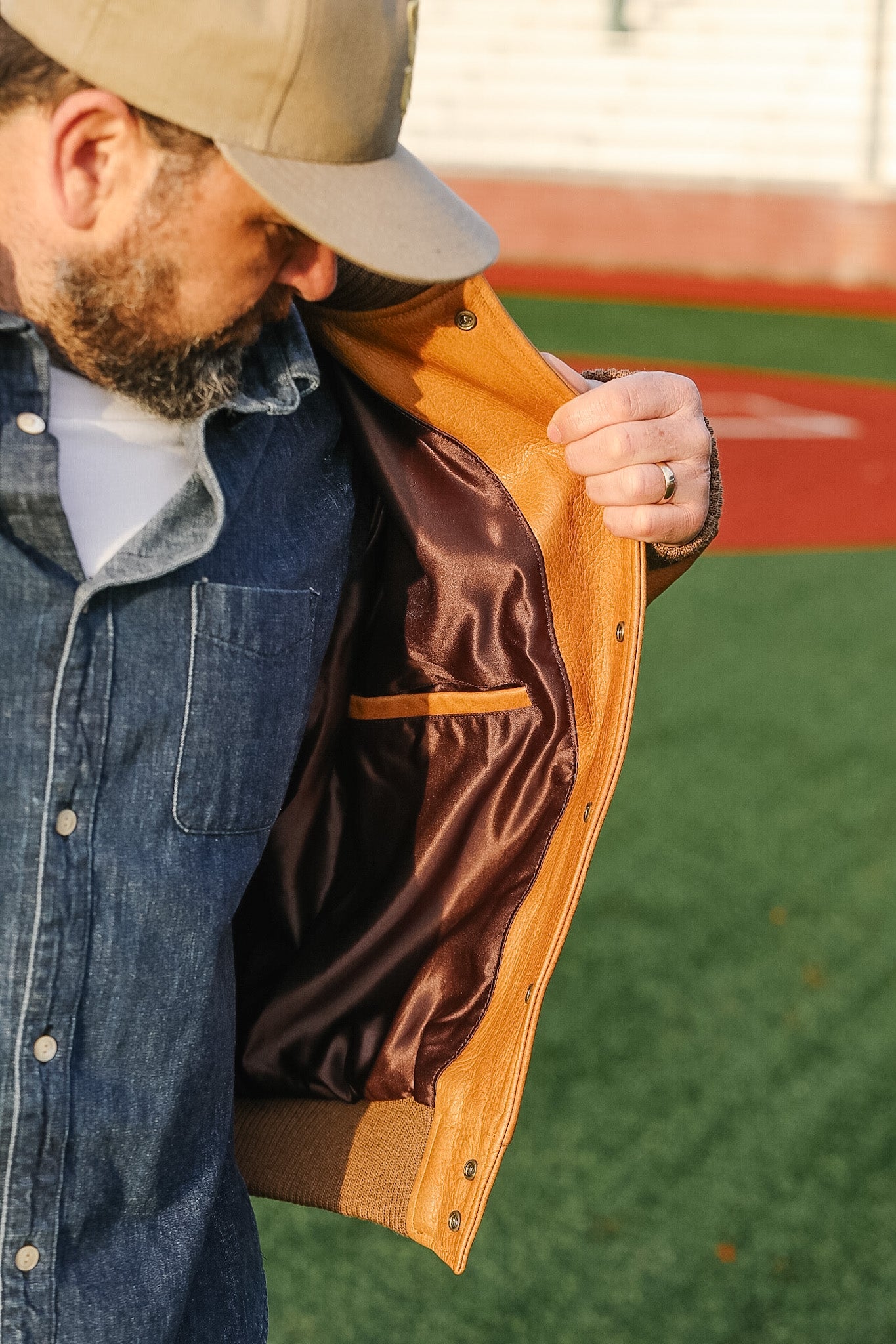 Man wearing a tan leather jacket over a denim shirt with a blurred background