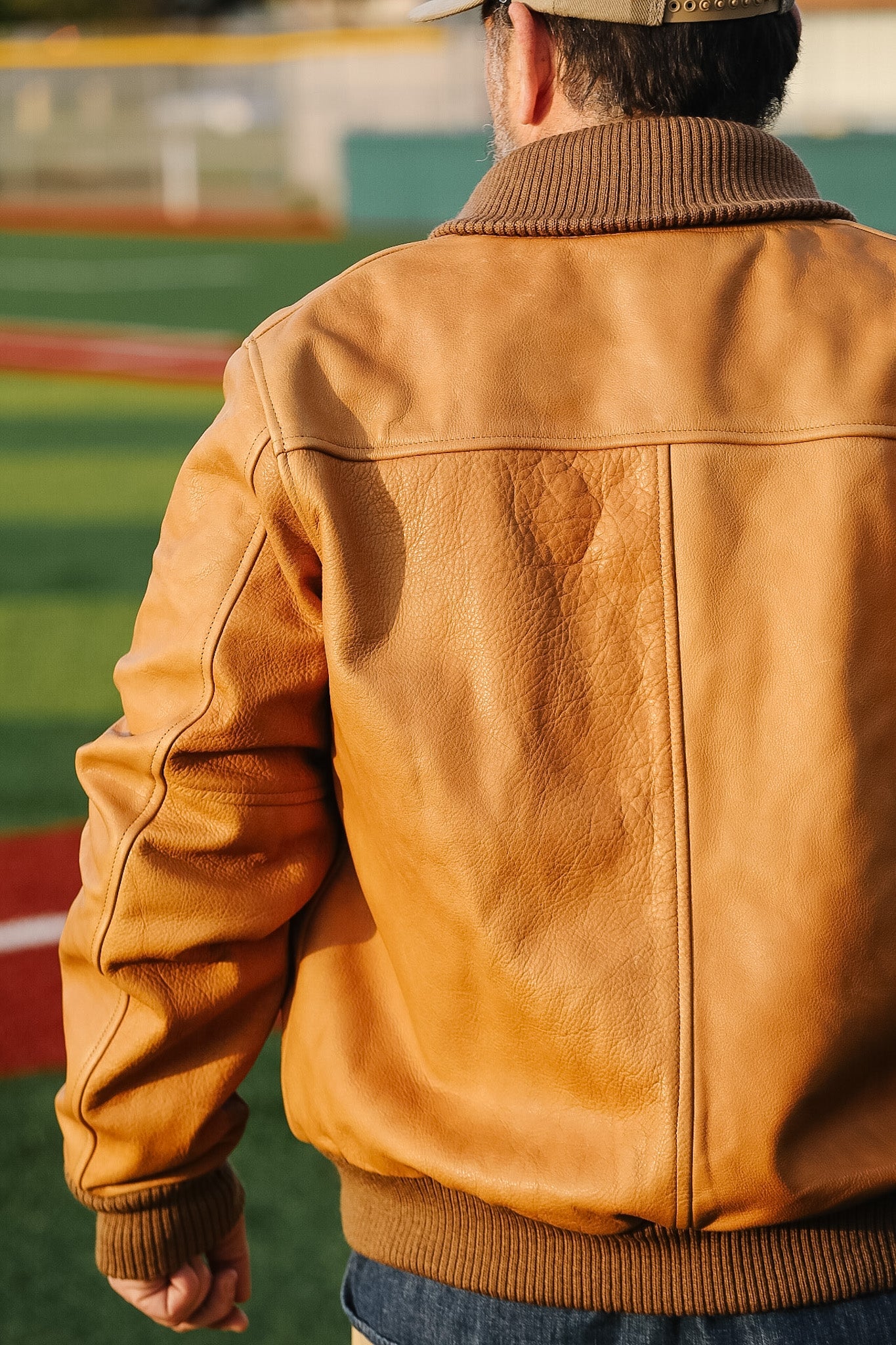Person wearing a brown leather jacket on a sports field