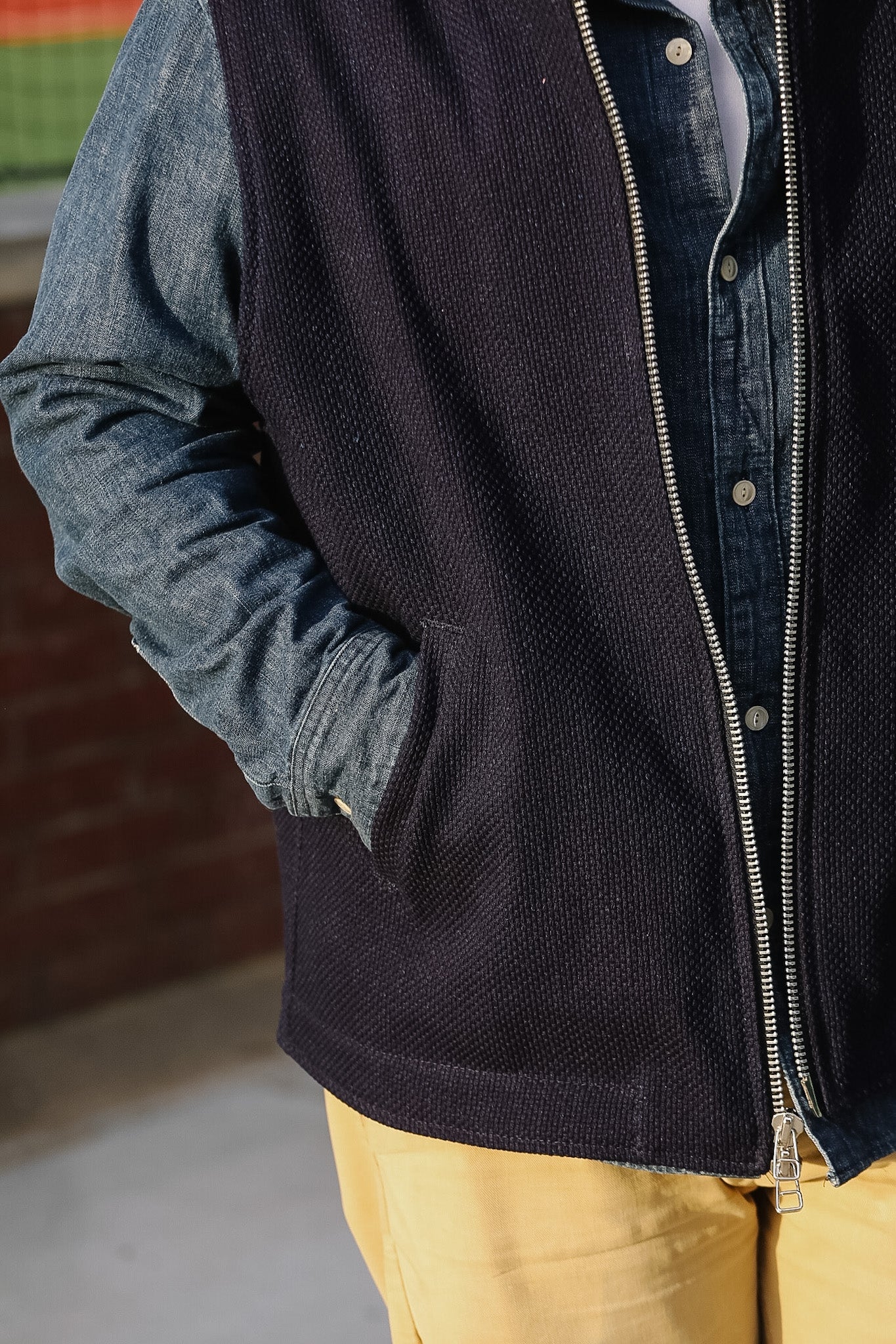 Person wearing a dark jacket with a zipper, blue shirt, and yellow pants.