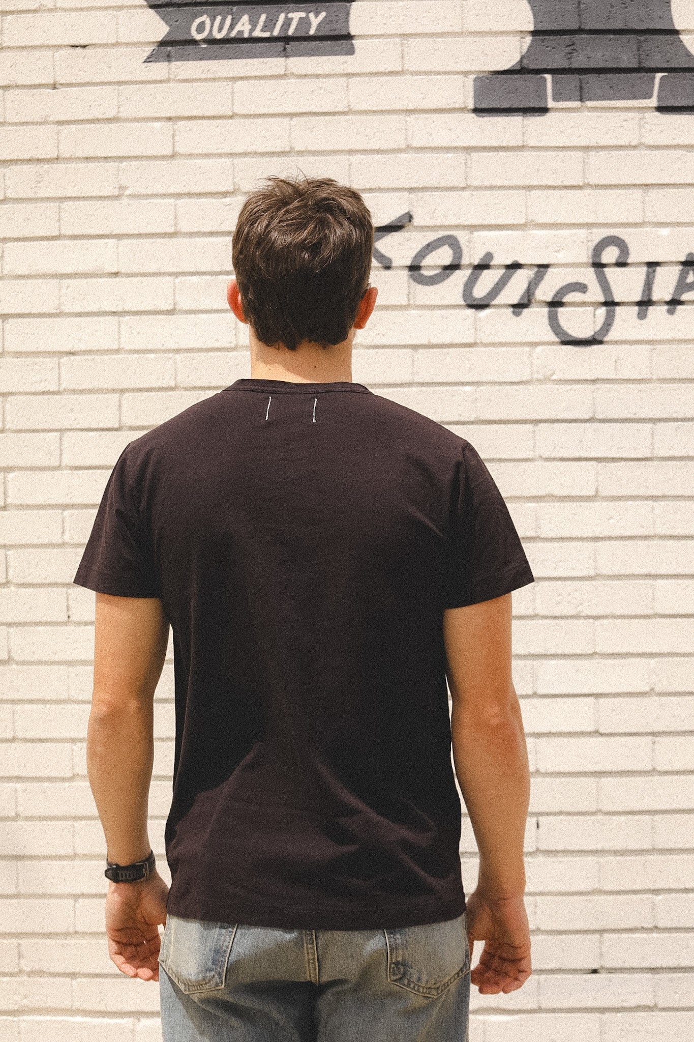 Man wearing a black t-shirt standing in front of a textured wall with graffiti.