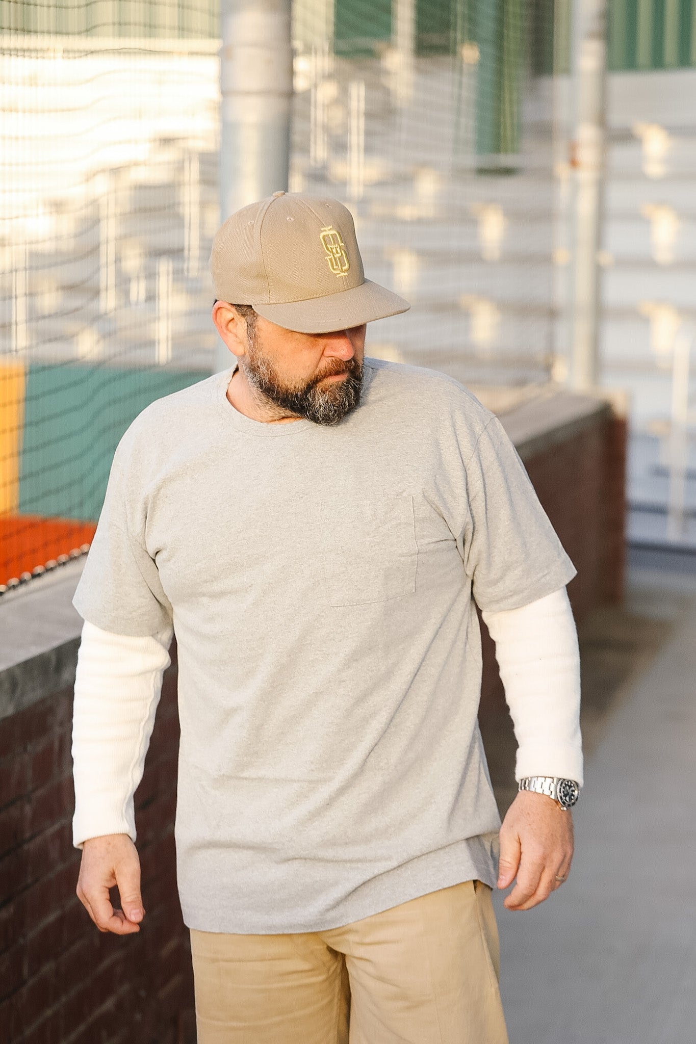 Man wearing a gray sweatshirt, beige cap, and beige pants on a rooftop.