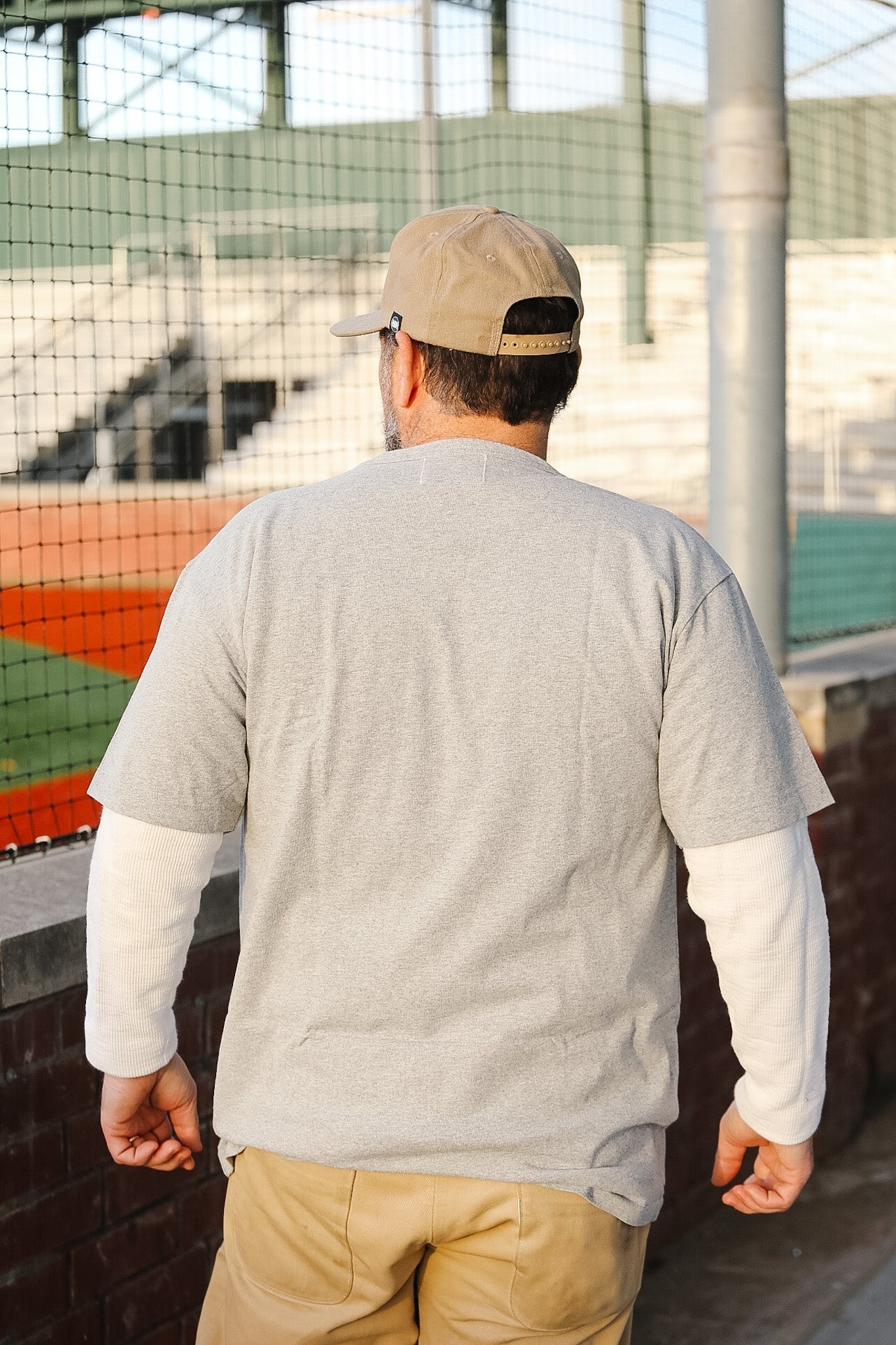 Man wearing a gray shirt and beige cap walking on a track or field.