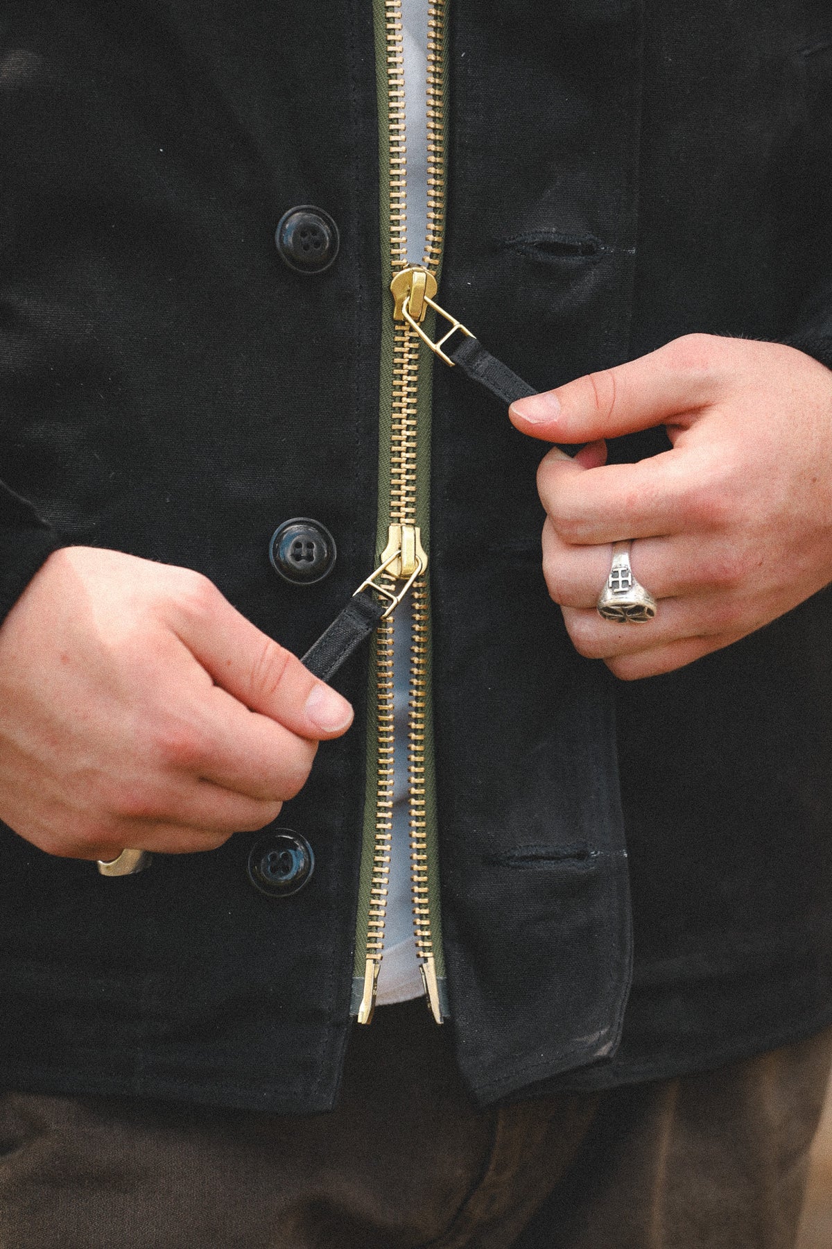 Close-up of a person's hands demonstrating a gold zipper with black rubberized teeth covers on a black jacket.