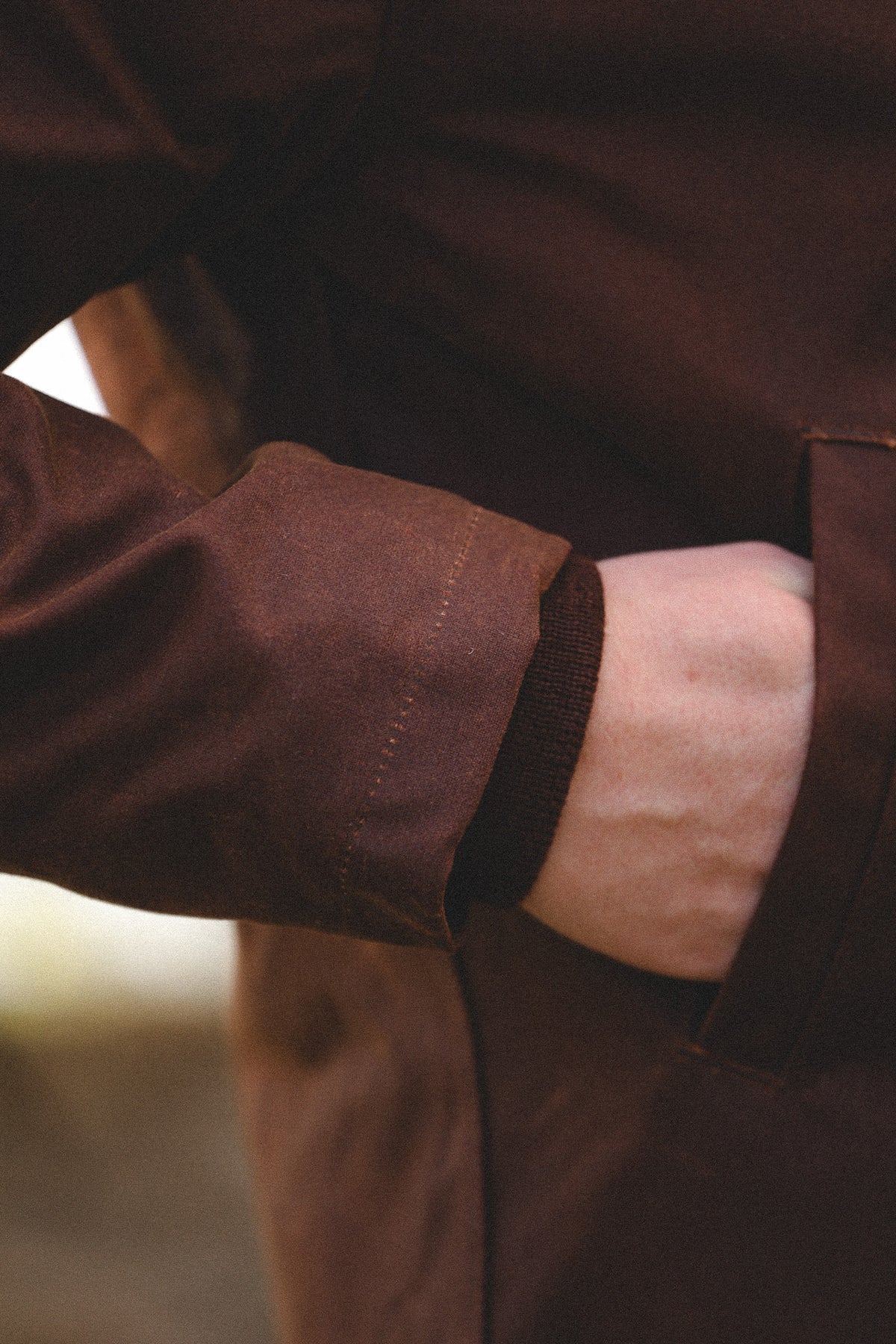 Close-up of a person wearing a dark brown jacket, showing the sleeve, cuff, and a hand tucked into a side pocket.