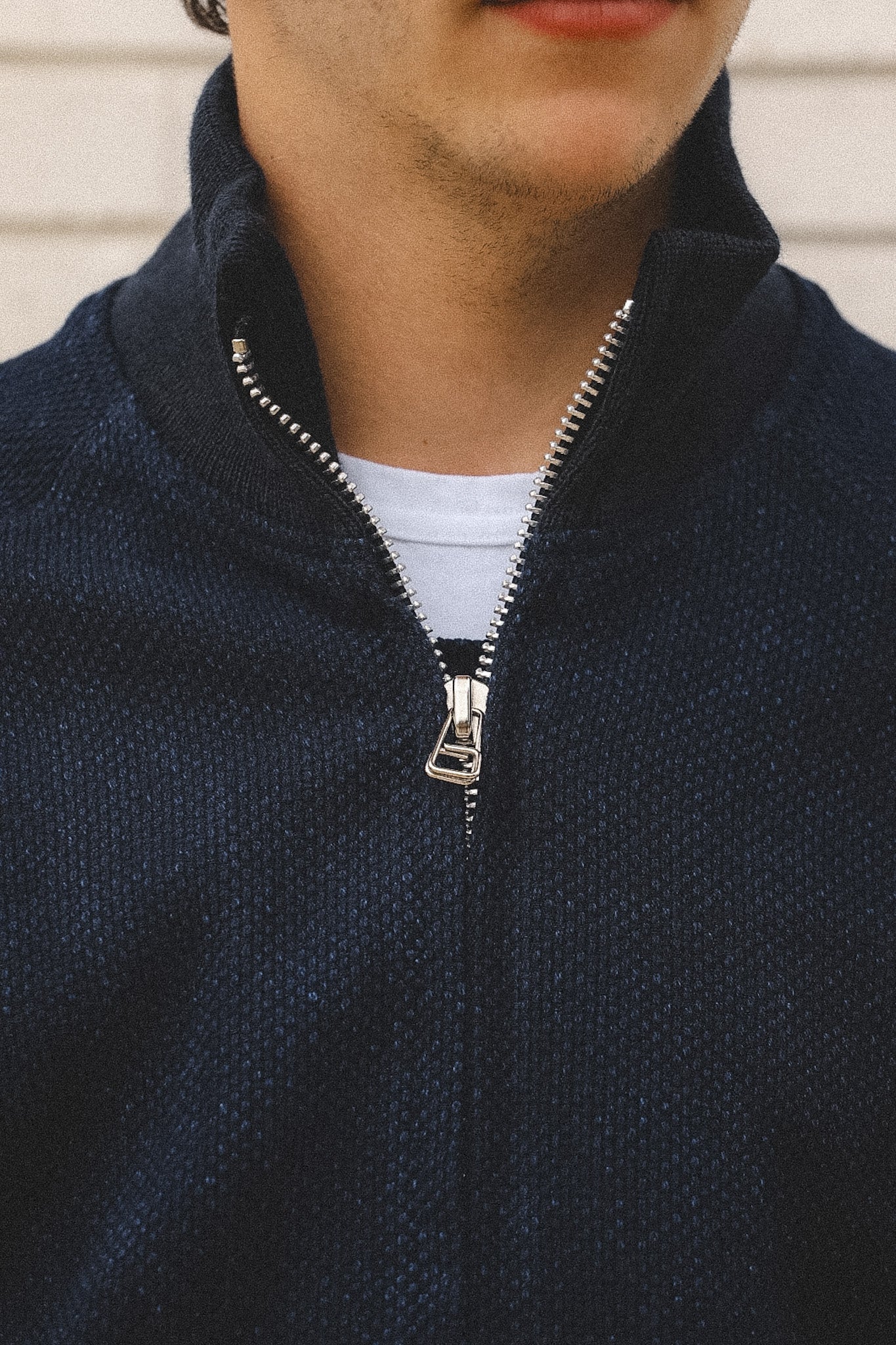 Close-up of a person wearing a navy blue zip-up sweatshirt with a beige background