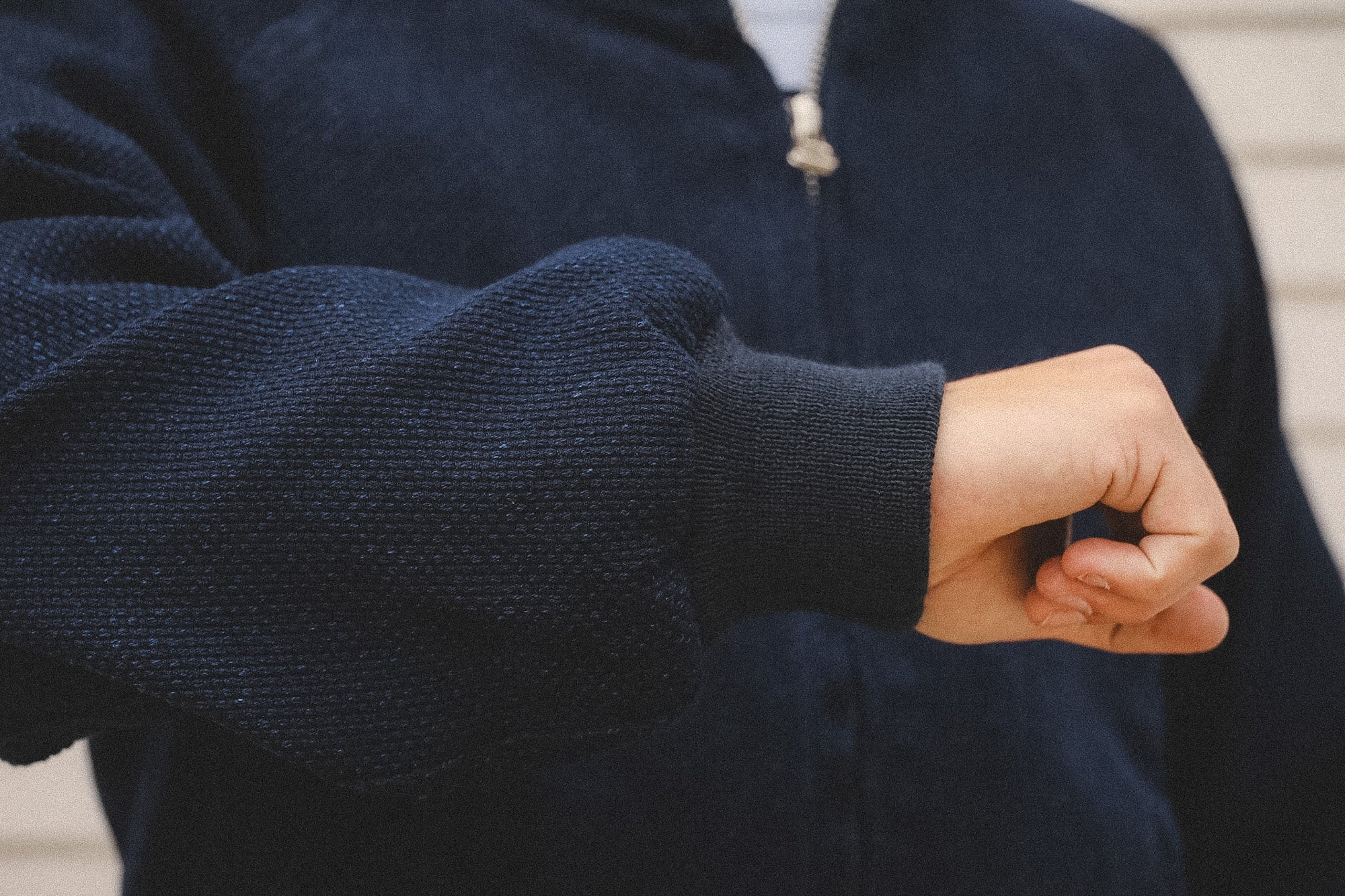 Person wearing a navy blue sweater with a close-up of the sleeve and hand.