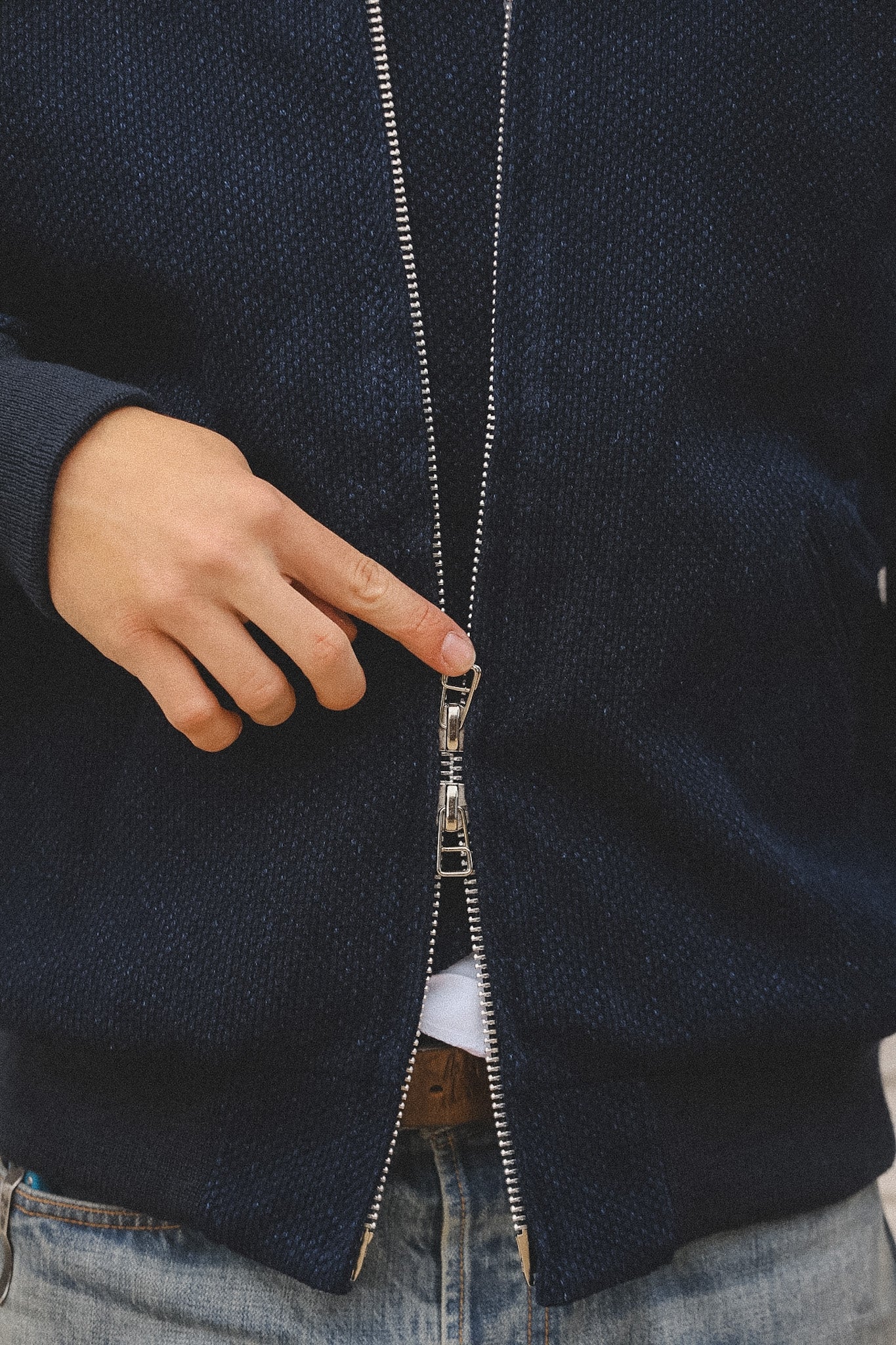 Close-up of a person zipping up a dark blue jacket with a white shirt peeking out.