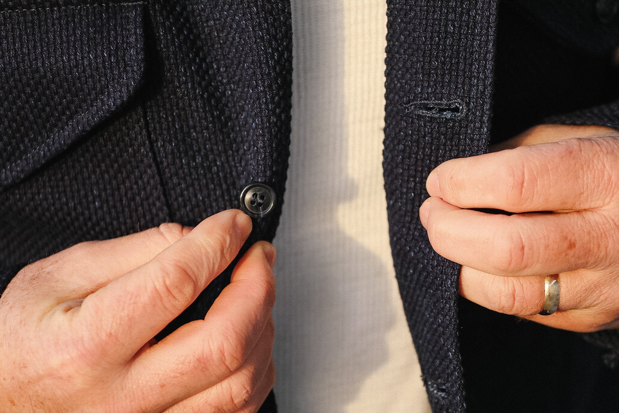 Close-up of hands buttoning a dark suit jacket.