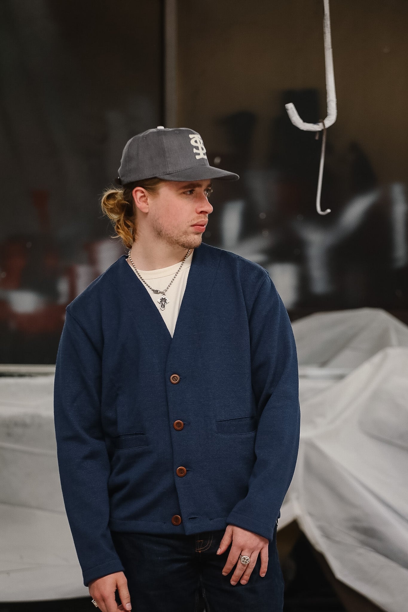 Man wearing a blue cardigan and cap standing in front of covered vehicles.