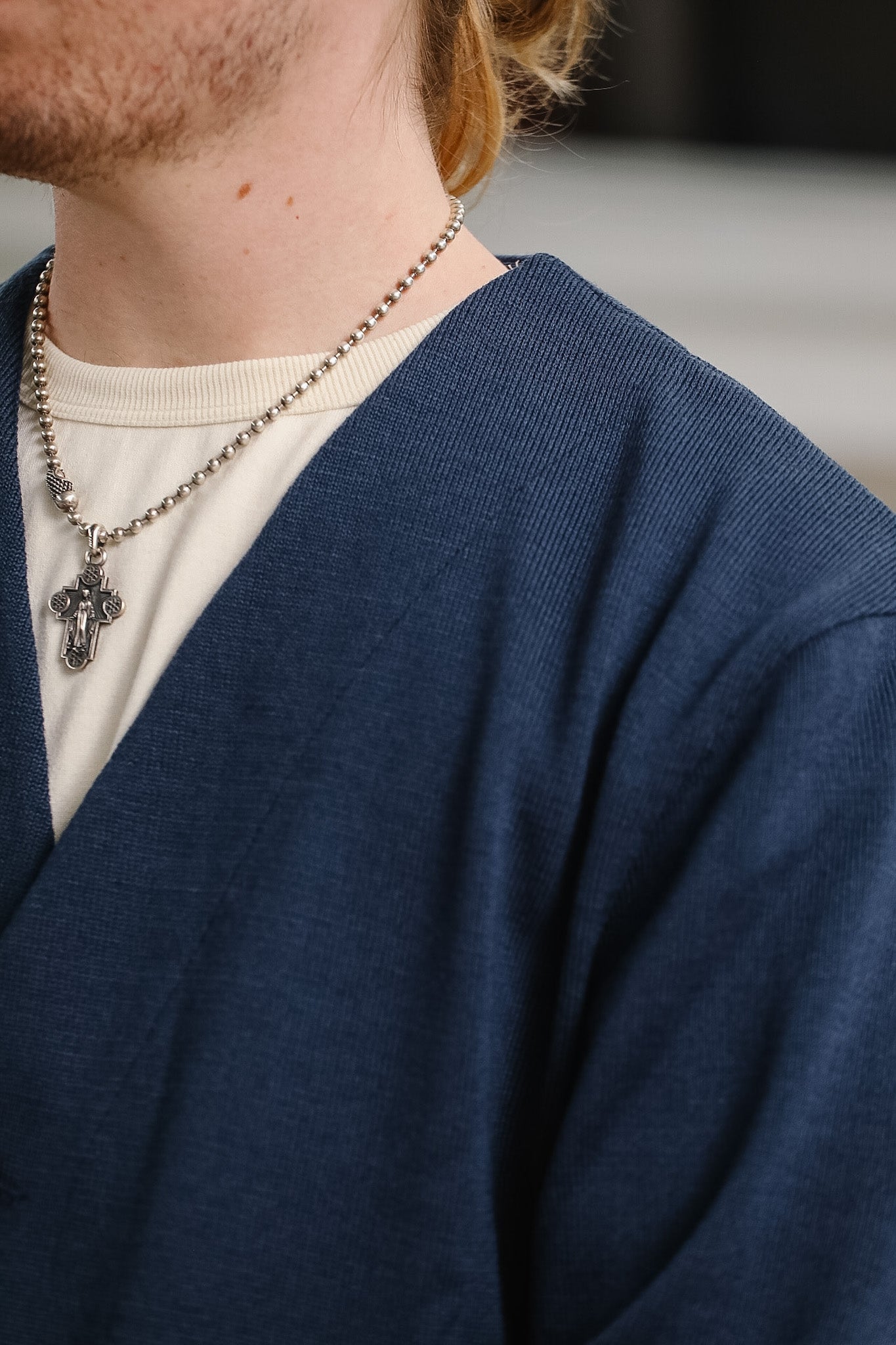 Person wearing a blue cardigan over a white shirt with a necklace featuring a cross pendant.