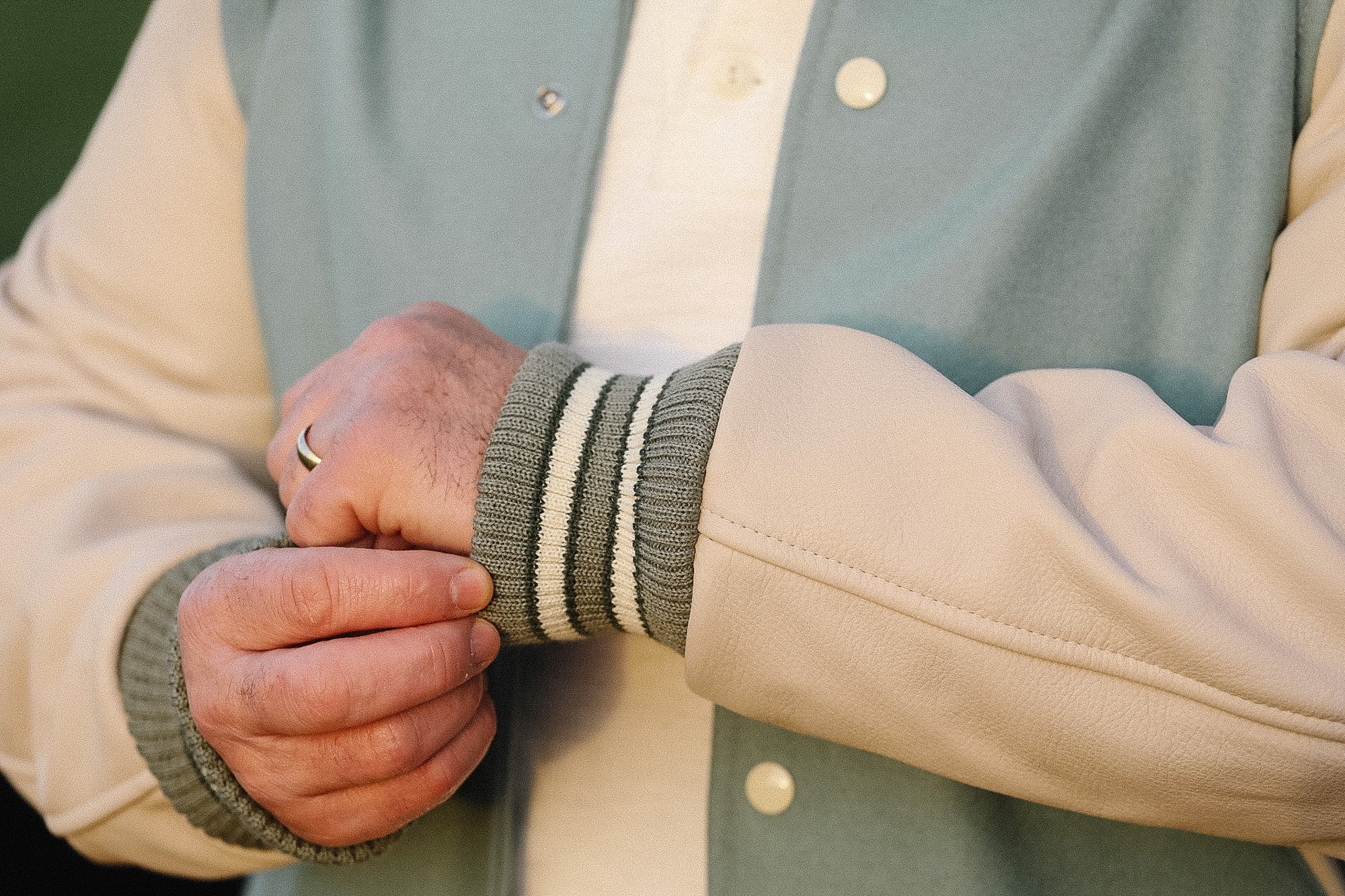 Close-up of a person wearing a beige and green varsity jacket with a focus on the sleeve and hands.