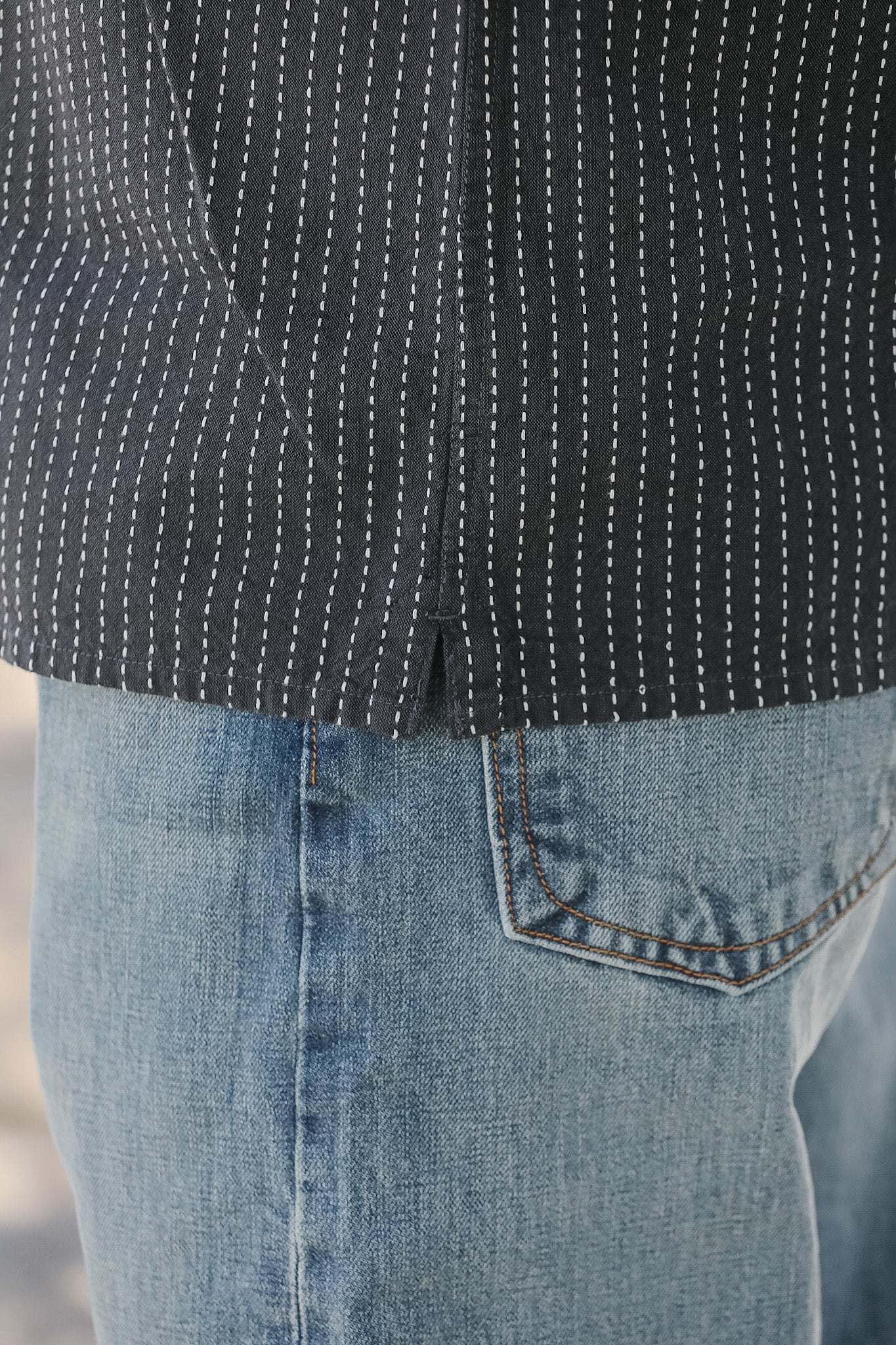 Close-up of a person wearing a black patterned shirt and blue jeans.