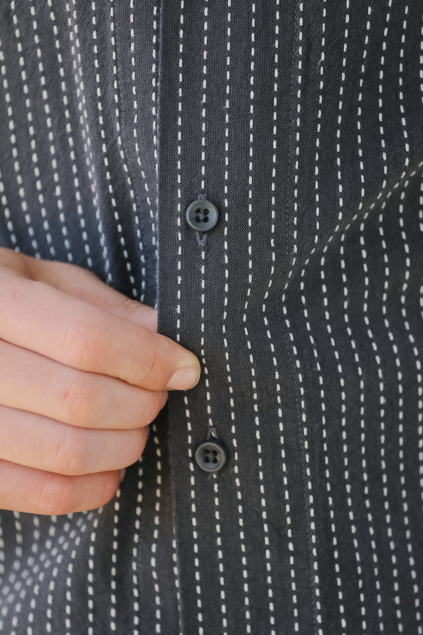 Close-up of a hand buttoning a black patterned shirt