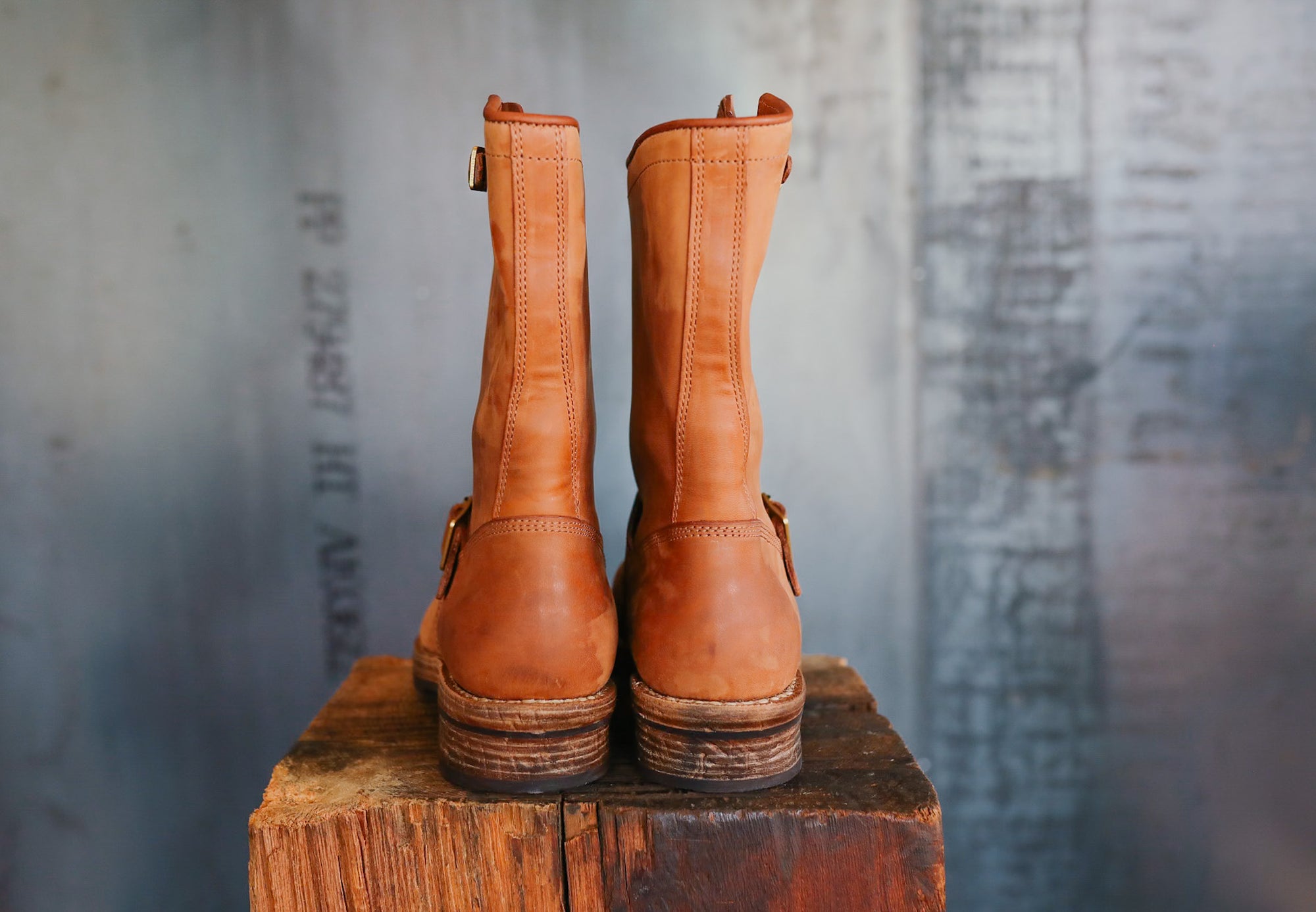 Pair of brown leather boots on a wooden block with a textured gray background