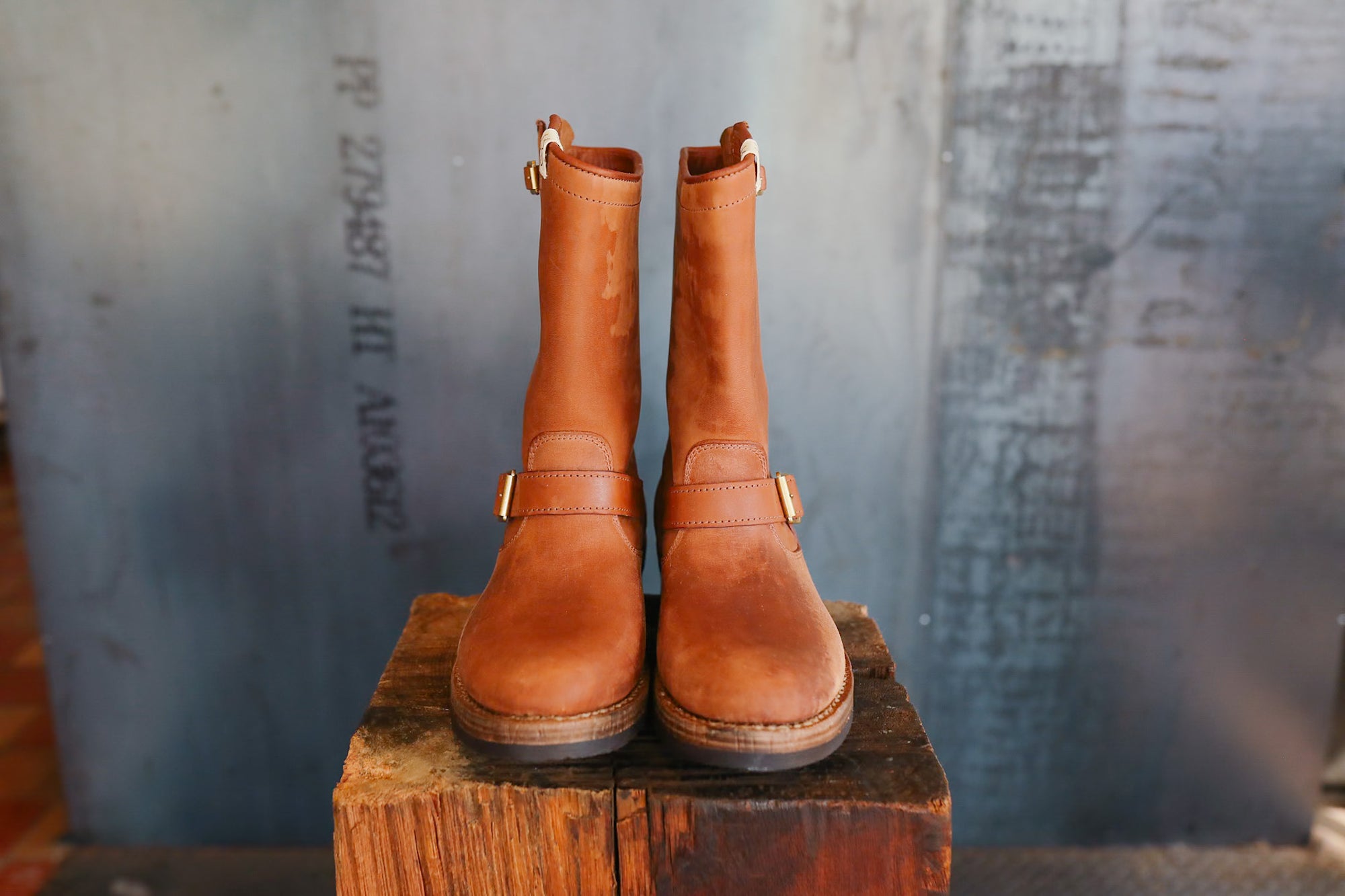 Pair of brown leather boots on a wooden block against a textured wall.