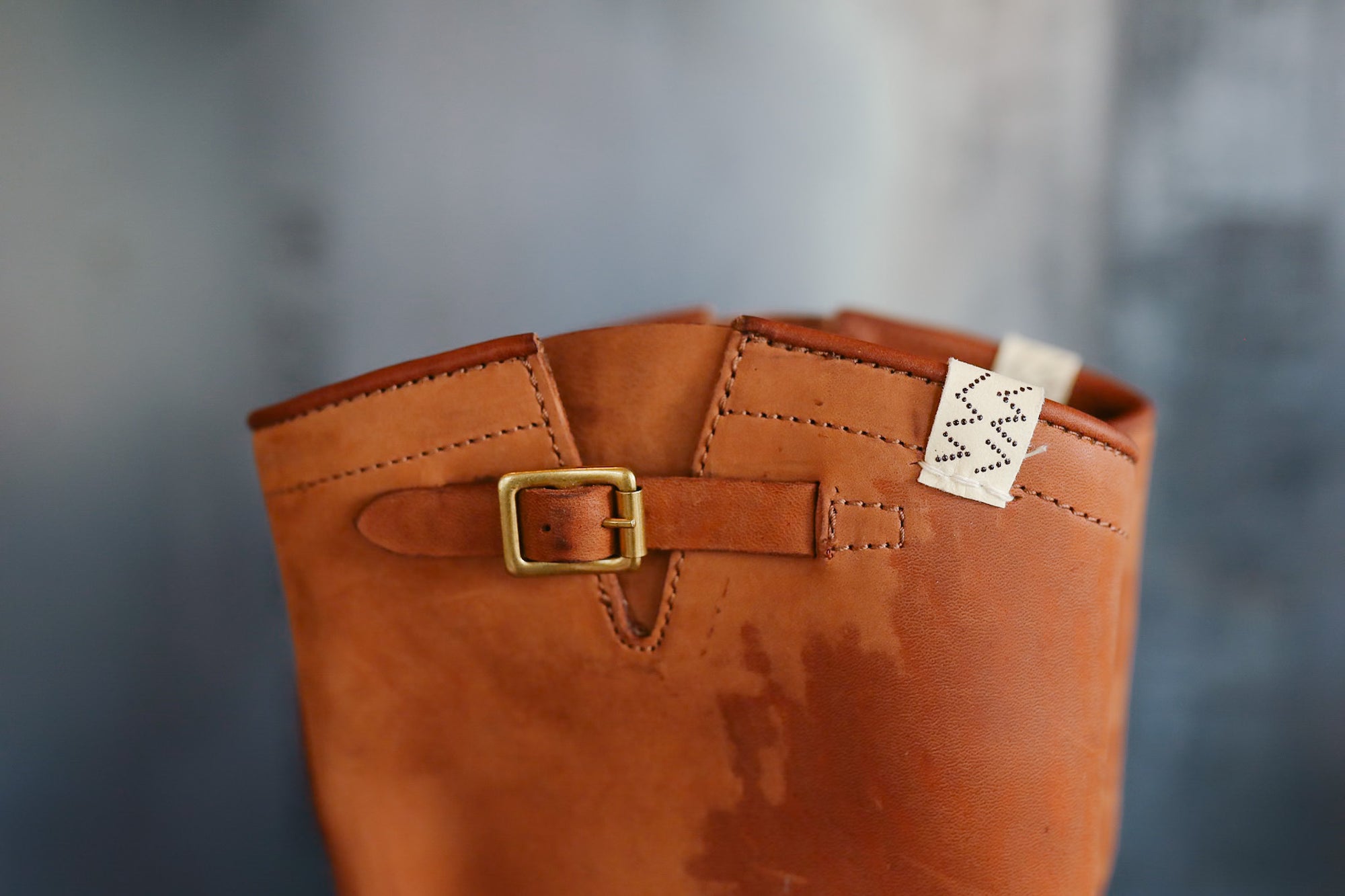 Brown leather boot with a gold buckle on a blurred background