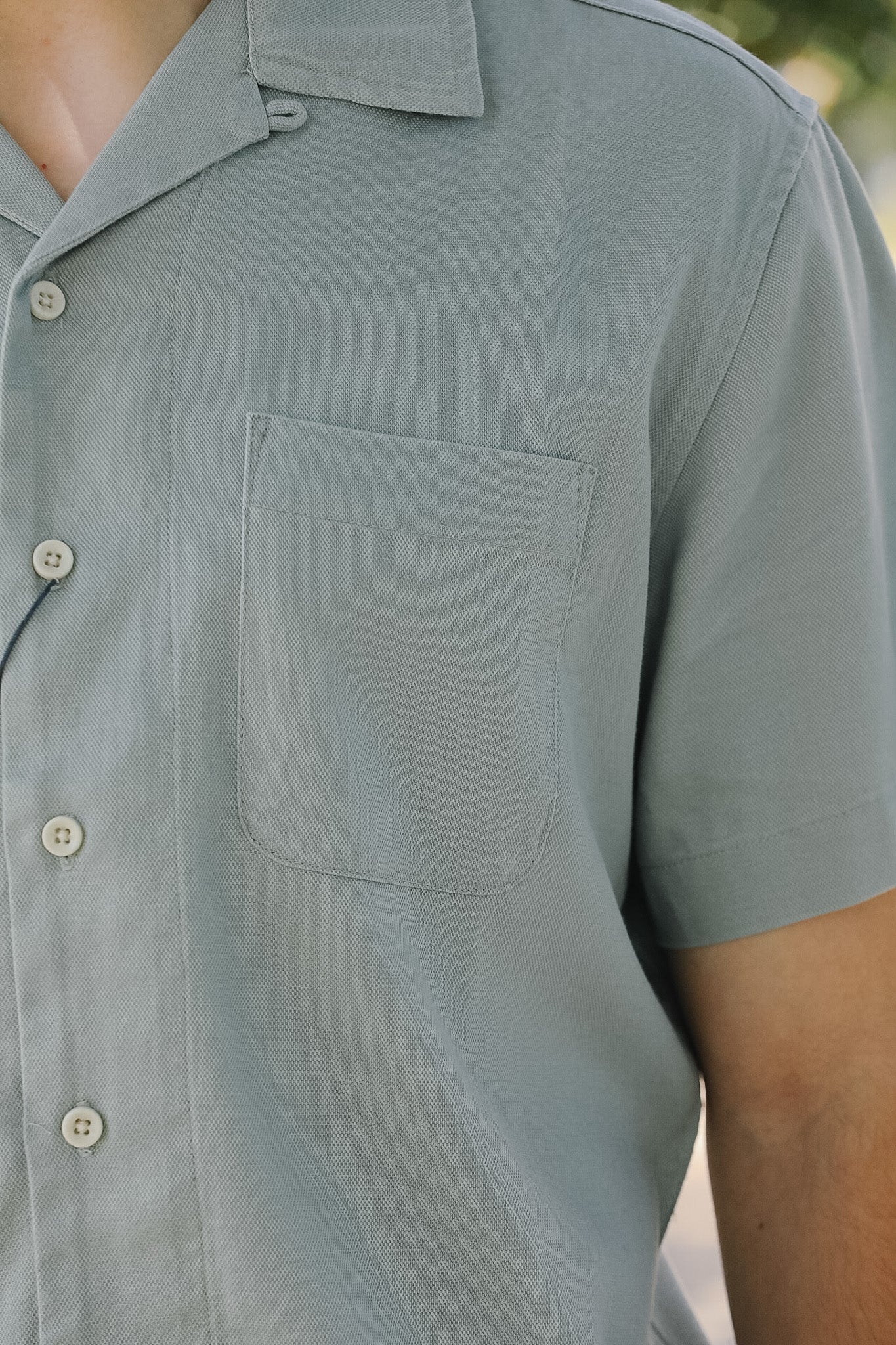 Close-up of a person wearing a light gray short-sleeve shirt with buttons.