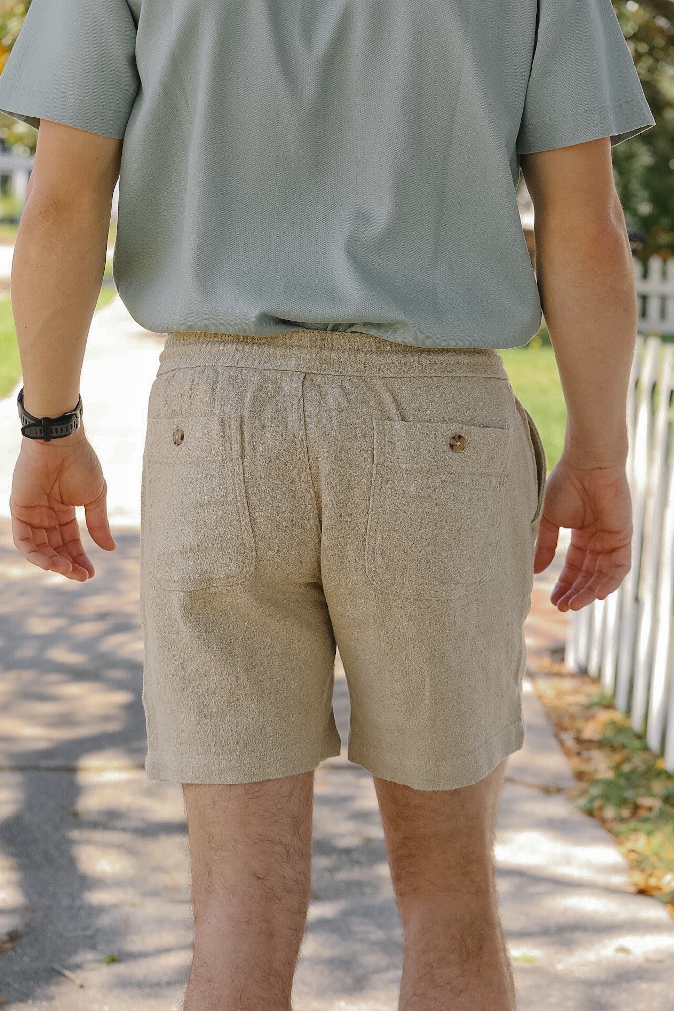 Person wearing a light gray shirt and beige shorts outdoors.