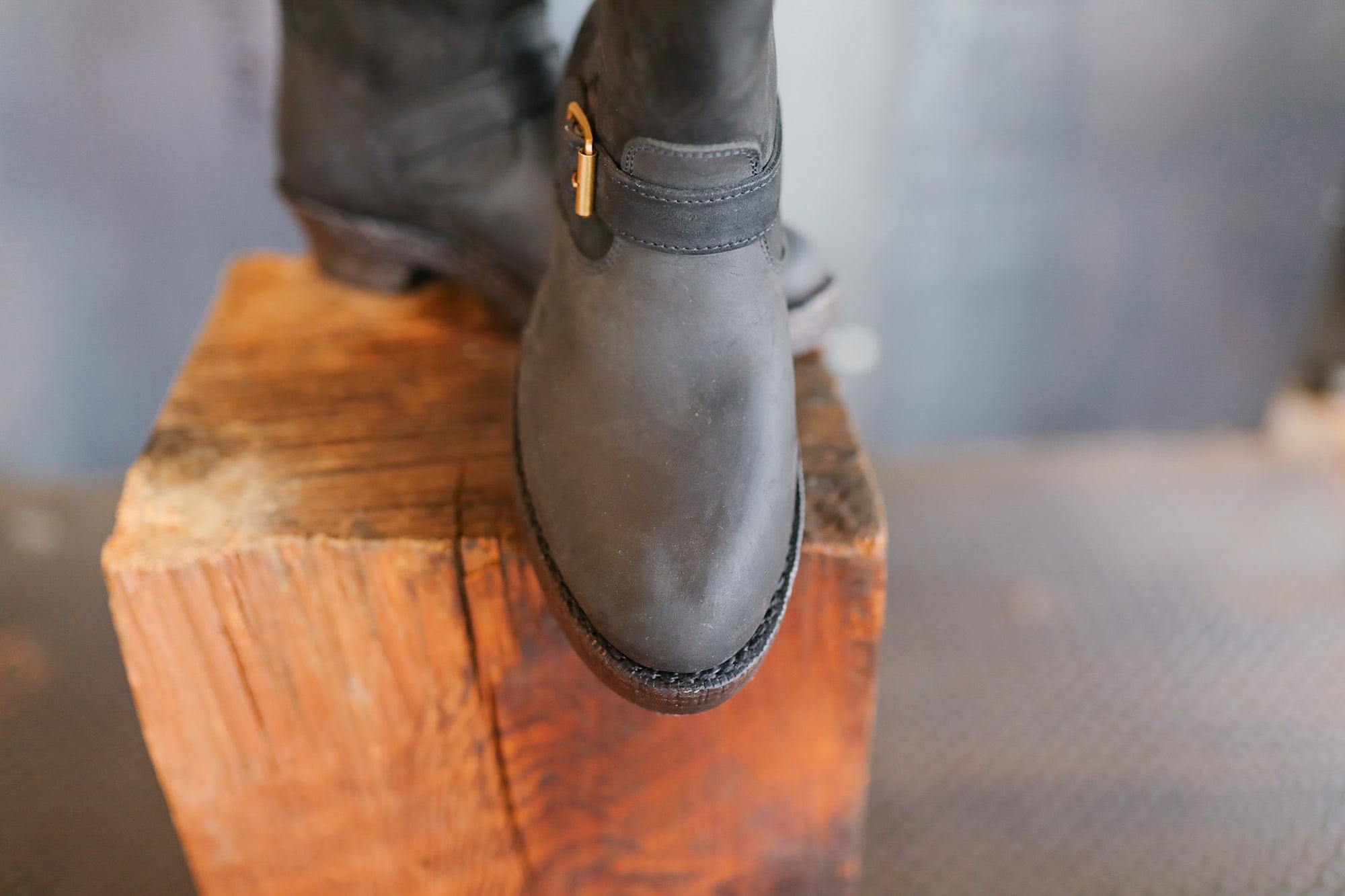 Black leather boot on a wooden block with a blurred background