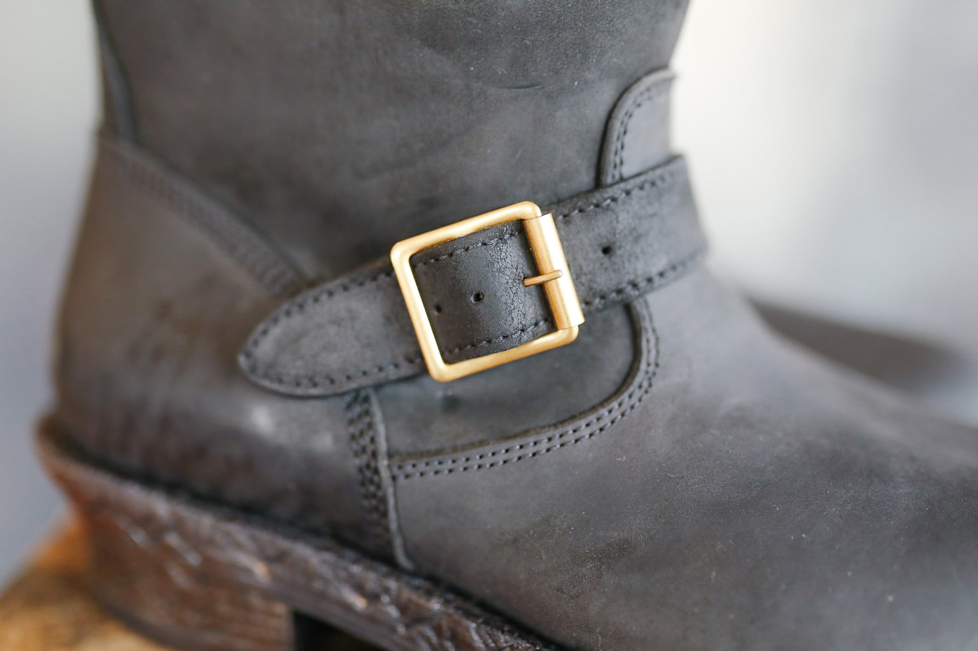 Close-up of a gray boot with a gold buckle on a blurred background