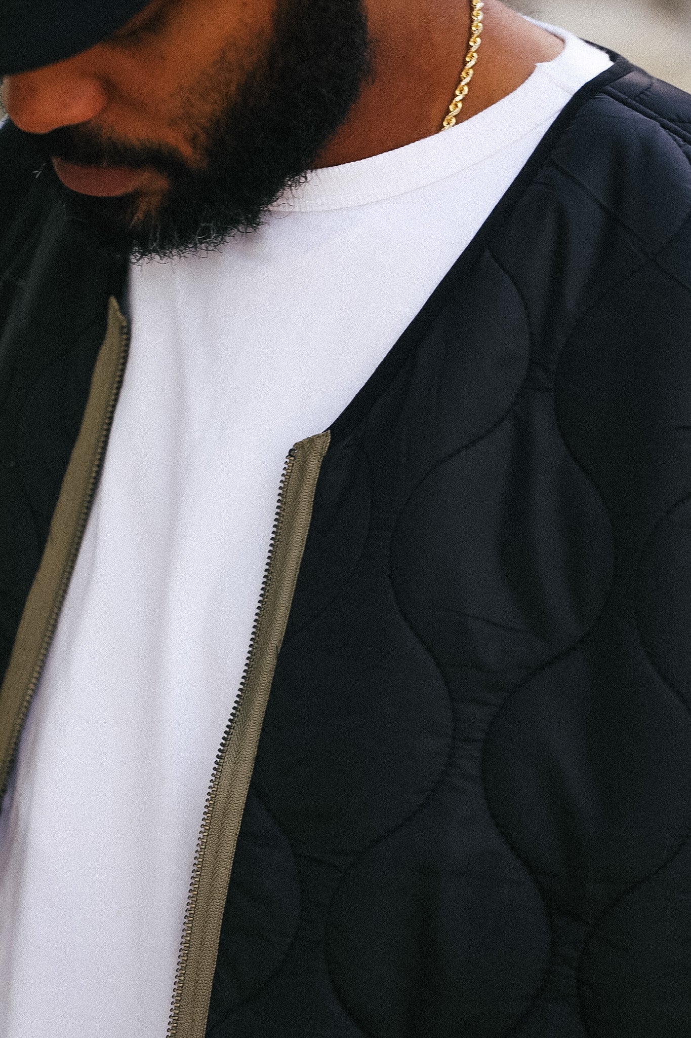 Close-up of a person wearing a black quilted jacket with a circular stitched pattern over a white t-shirt, accessorized with a gold chain necklace.