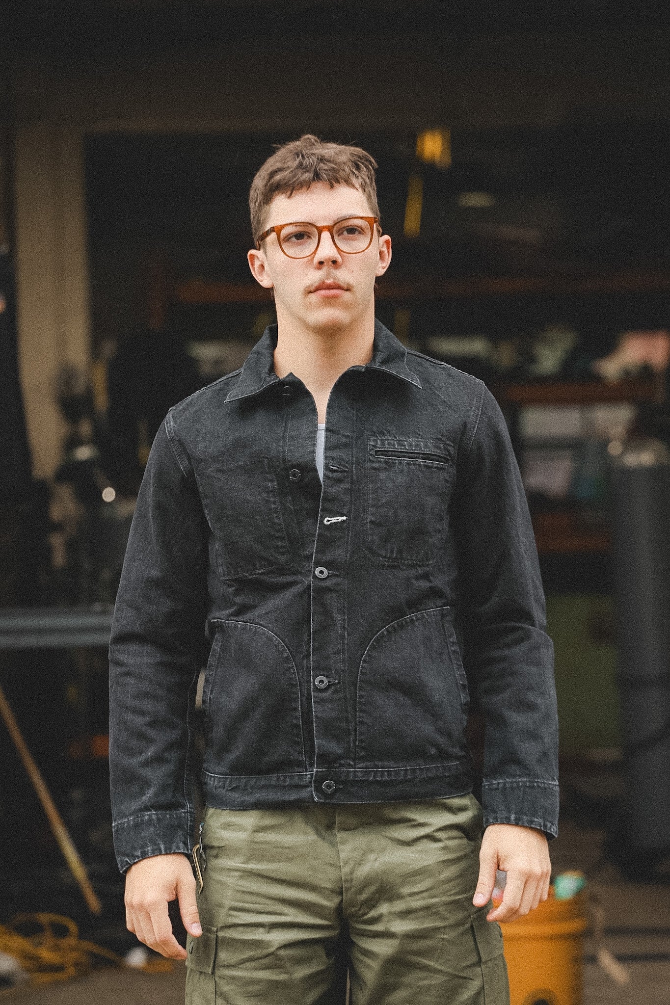 Person wearing a dark denim jacket and green pants in an indoor setting