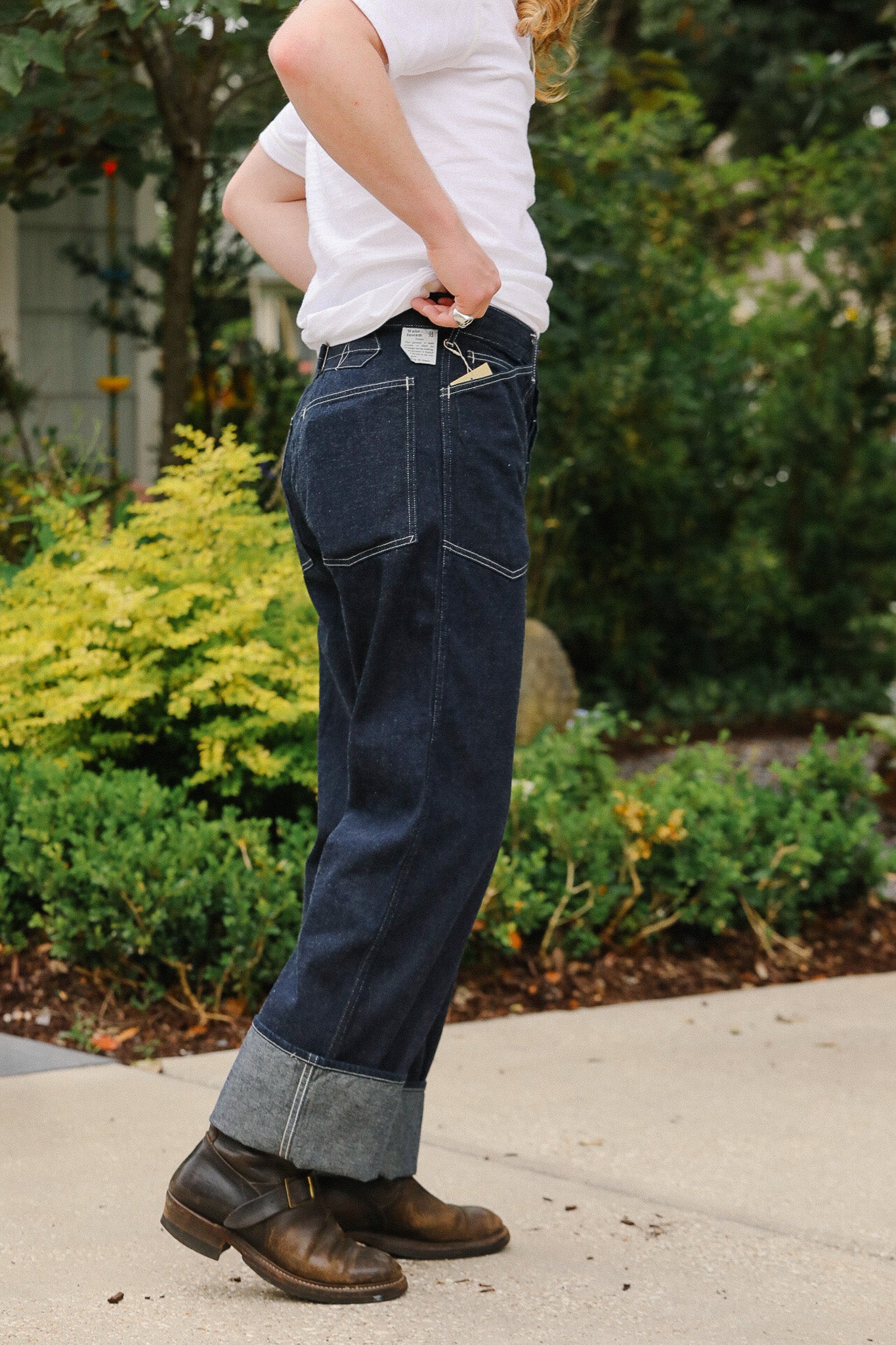 Person wearing blue jeans and a white shirt outdoors with greenery in the background