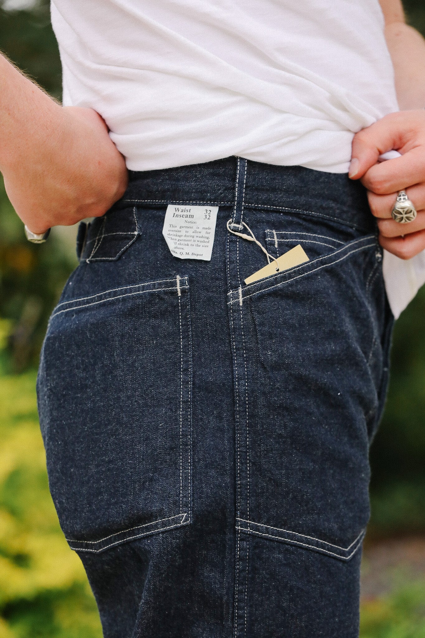 Person wearing dark blue jeans with a visible brand tag, standing outdoors.