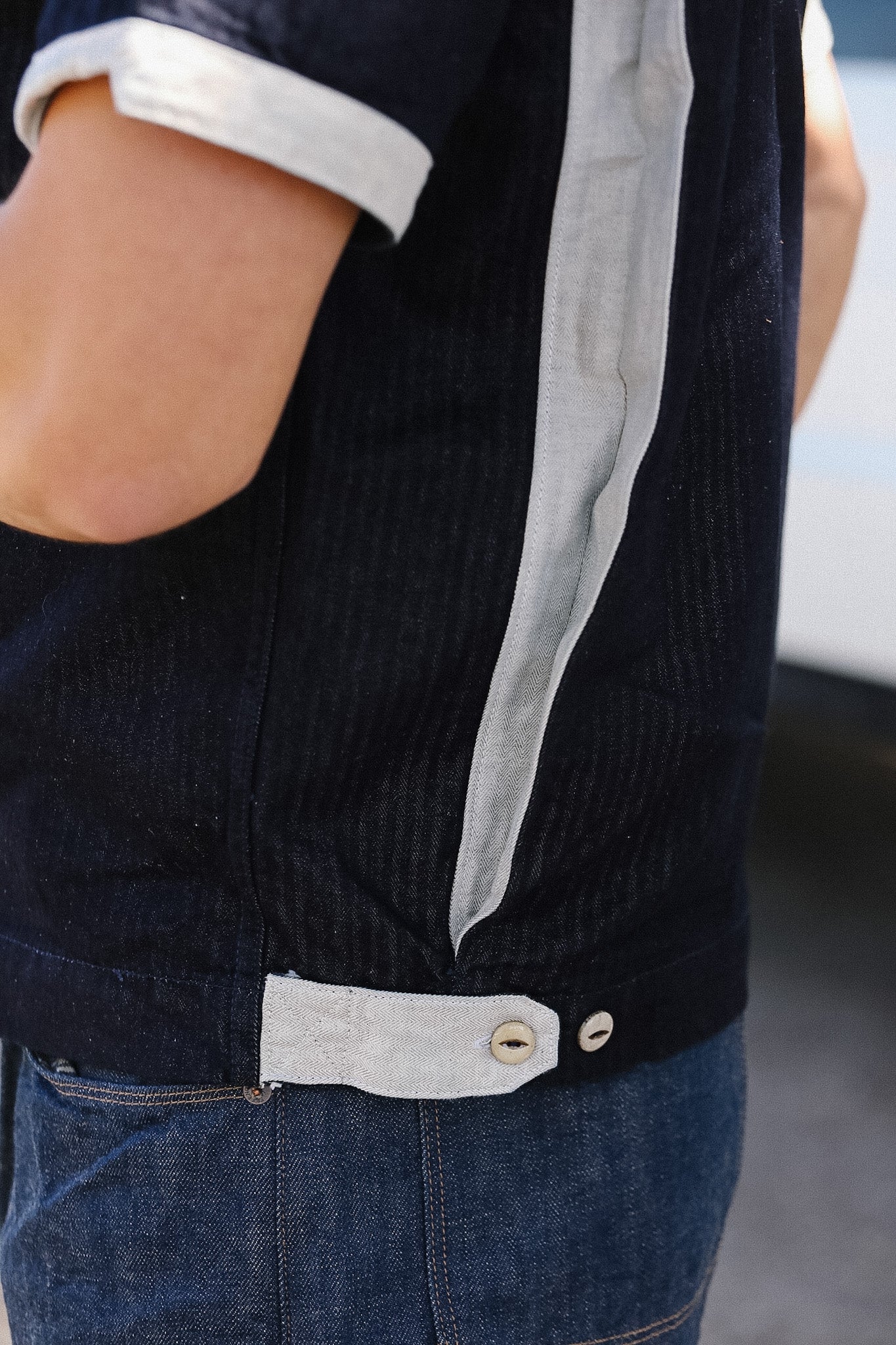 Close-up of a person wearing a dark jacket with a light gray stripe and blue jeans.