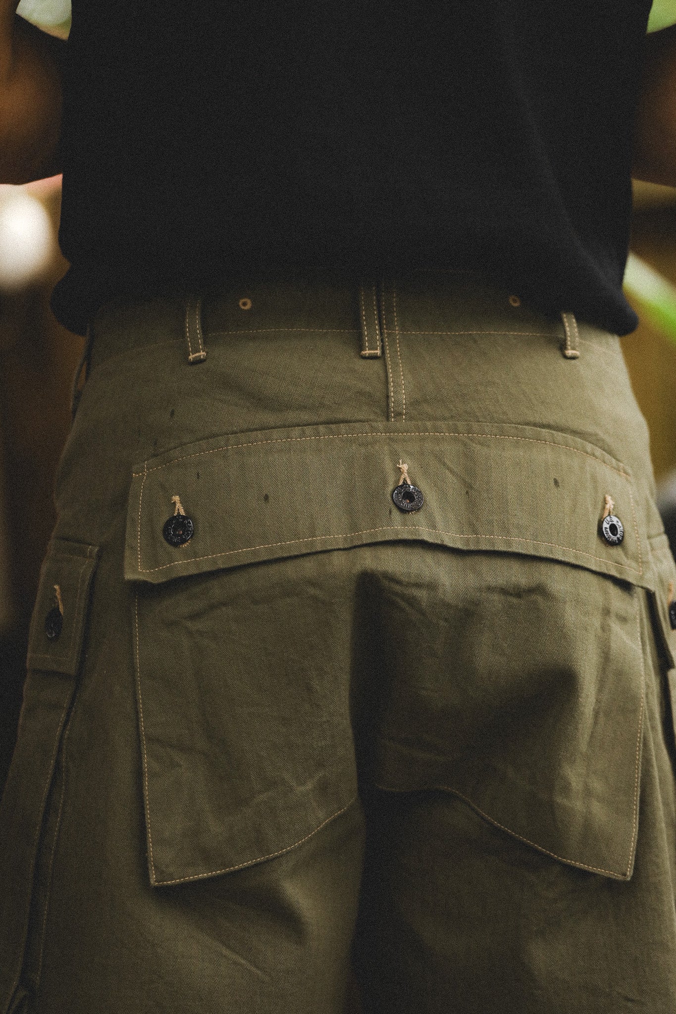Person wearing olive green pants with multiple pockets and buttons.