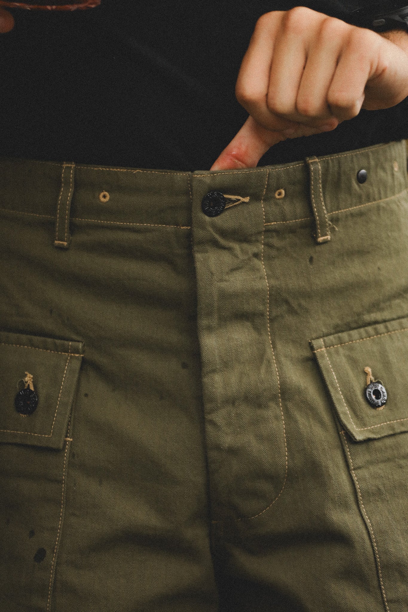 Close-up of olive green pants with pockets and buttons.
