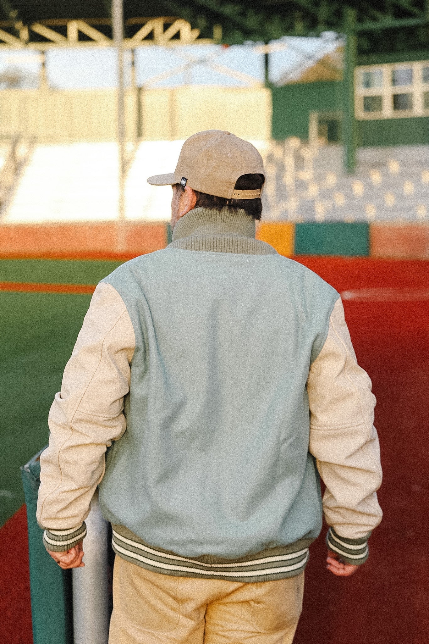 Person wearing a two-tone jacket and cap walking on a sports field.