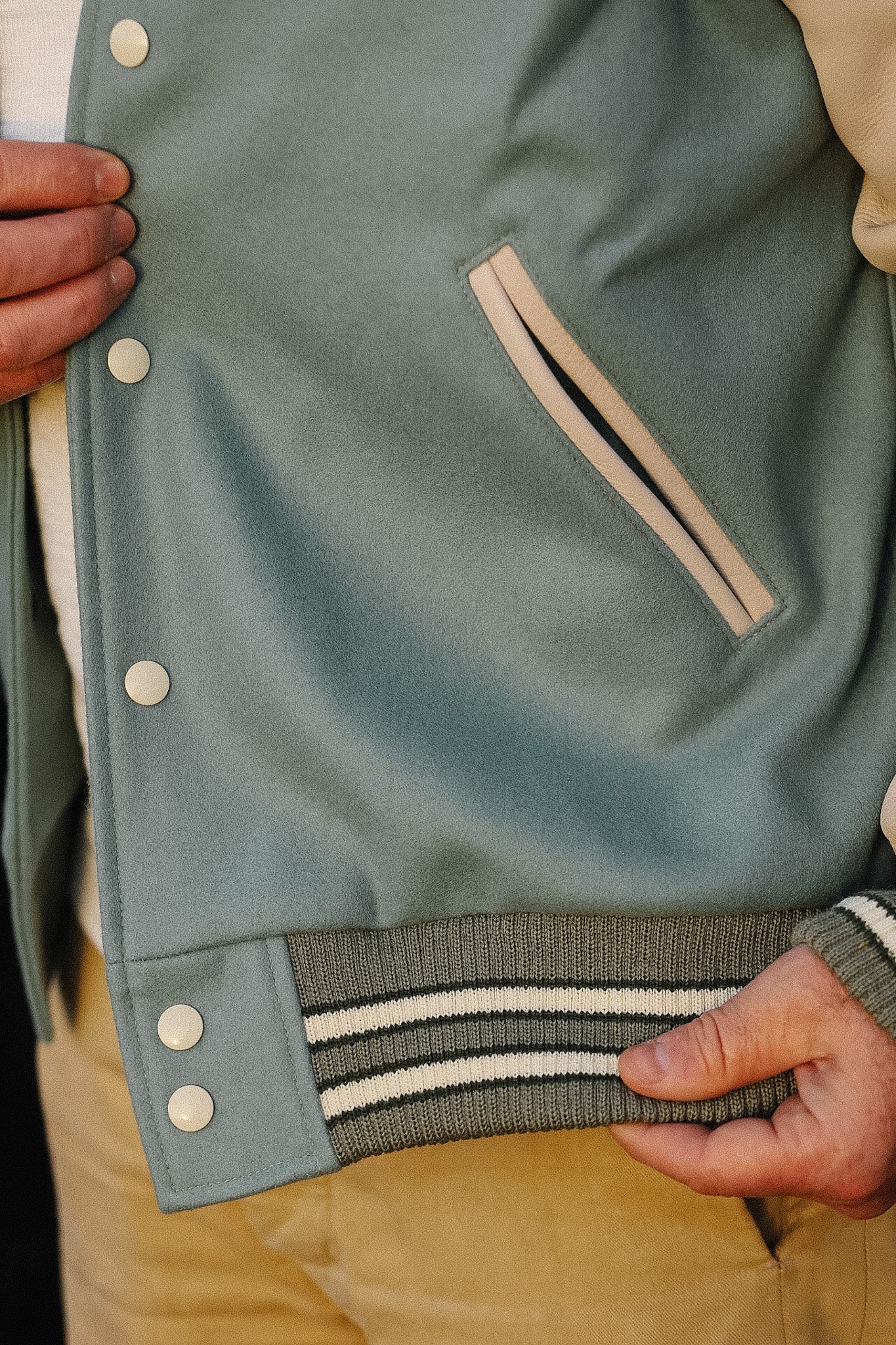 Close-up of a person holding a green varsity jacket with a beige interior lining.