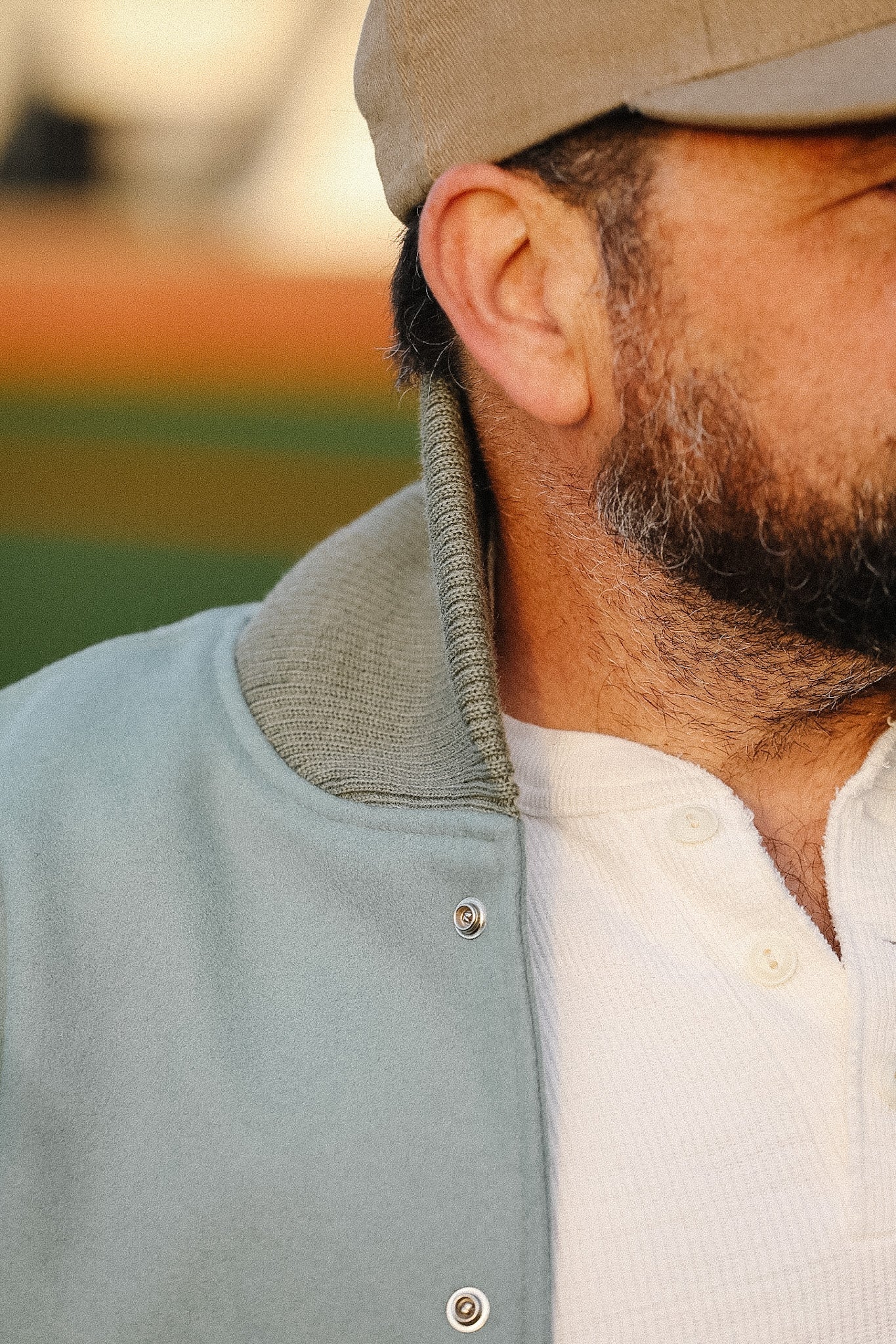 Close-up of a person wearing a light blue jacket and beige cap with a blurred background