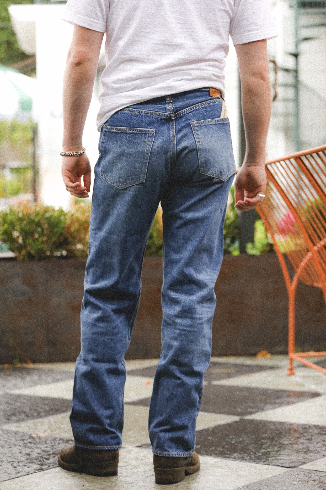 Person wearing blue jeans and a white shirt outdoors on a checkered floor.