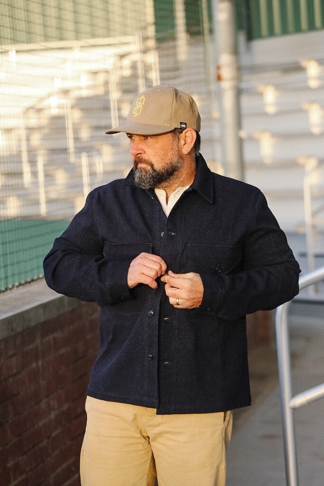 Man wearing a dark jacket and beige cap standing outdoors near a building.