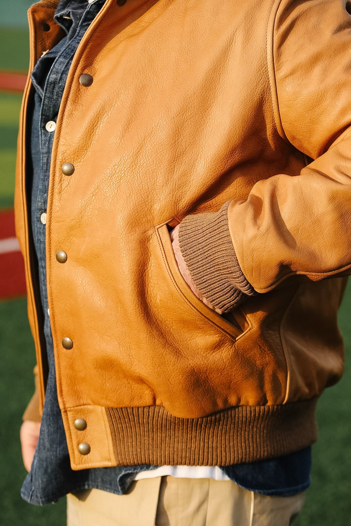 Close-up of a brown leather jacket with a person wearing it outdoors.