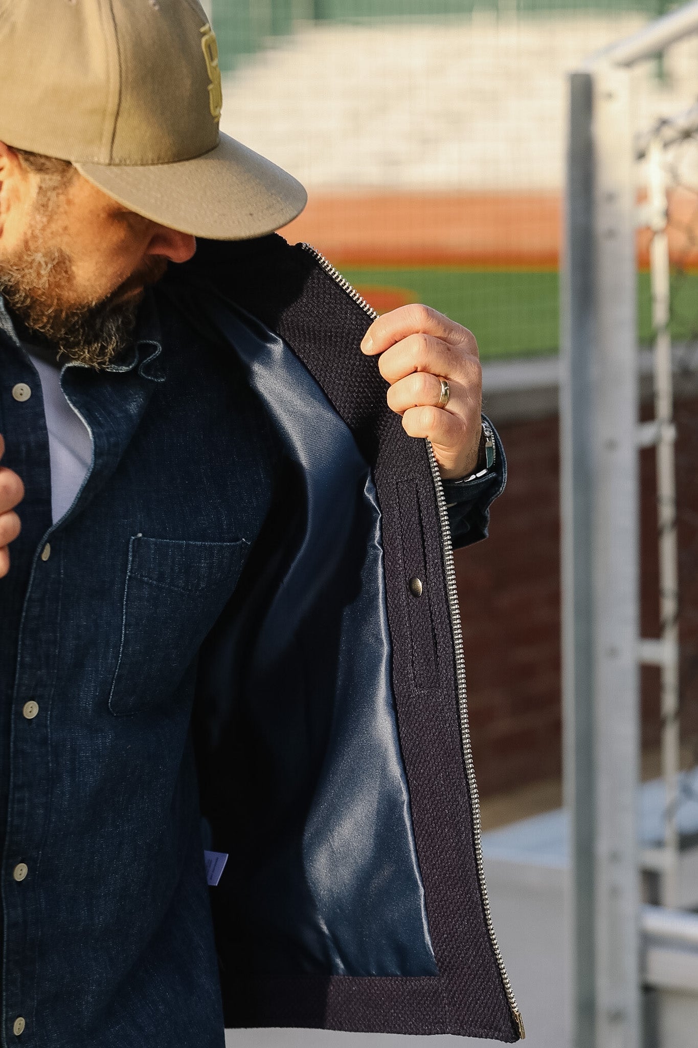 Man wearing a beige cap and dark jacket with a blurred outdoor background