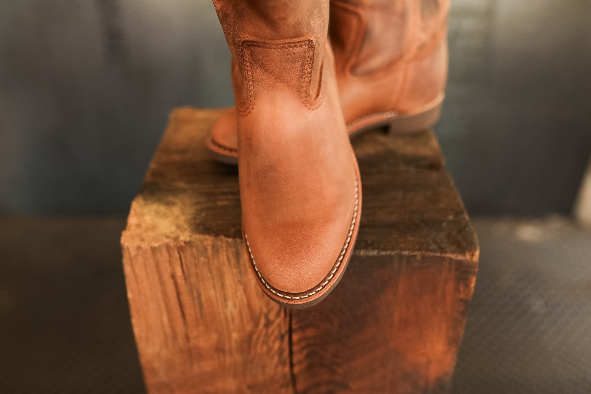Brown leather boot on a wooden block with a blurred background
